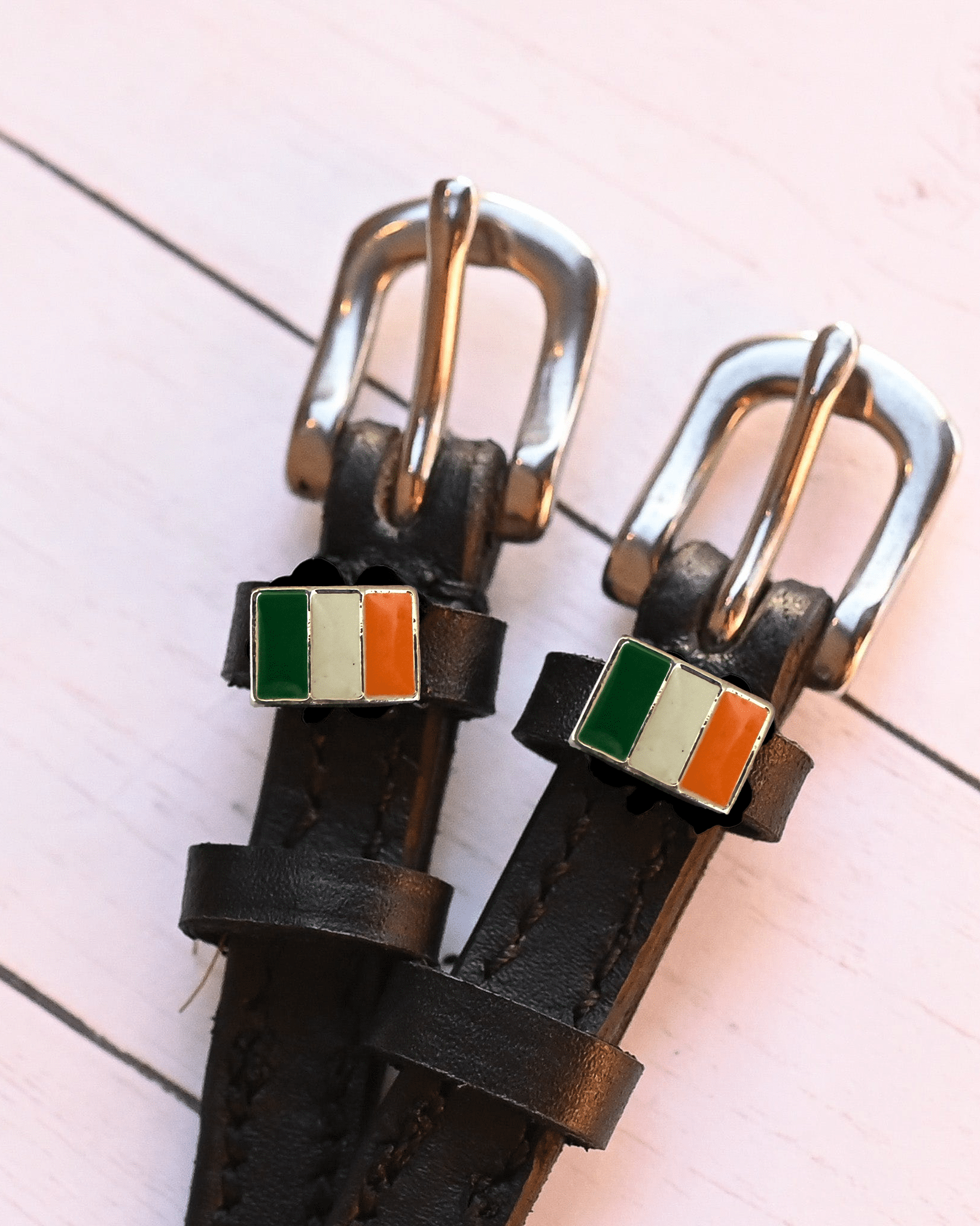 Angled close-up of Irish flag charms on ManeJane spur straps over pink planks