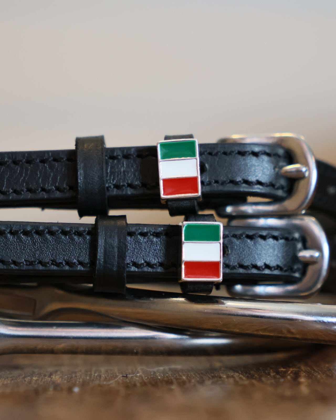 Close-up of a green-white-red Italian flag charm on black leather spur straps