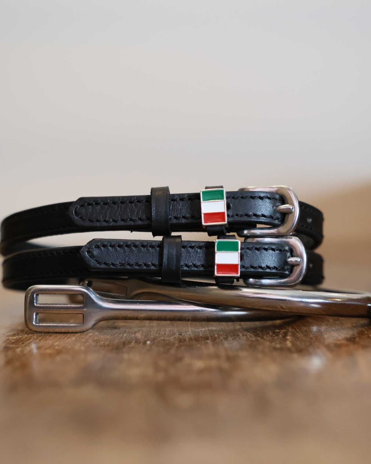 Black leather Italian flag spur straps coiled beside a spur on wood