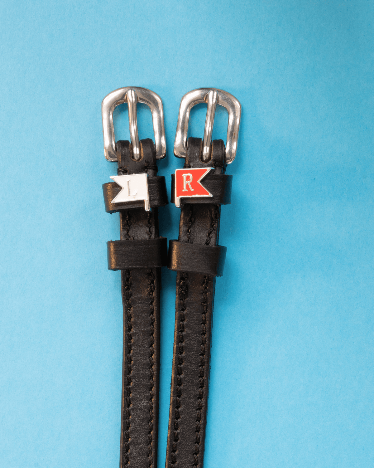 Black leather spur straps with silver buckles and white L and red R jump-flag charms on blue