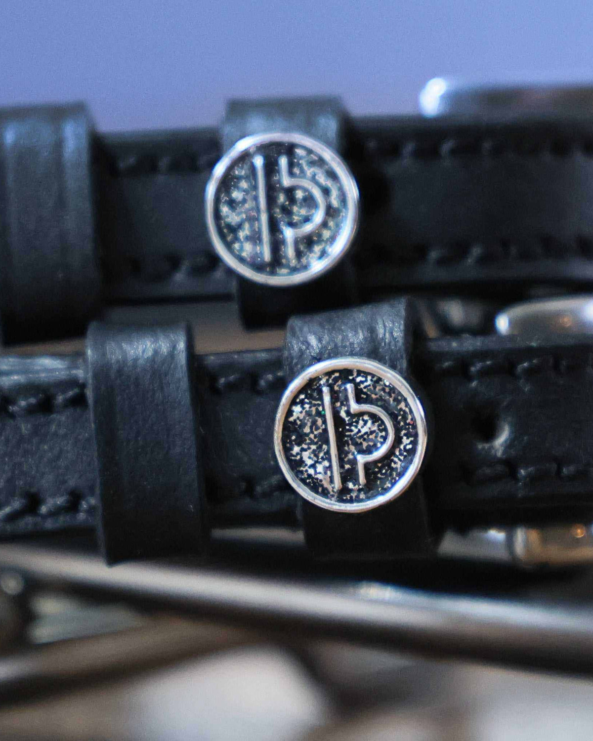 Close-up of silver Libra zodiac coin charms on black leather spur strap keepers