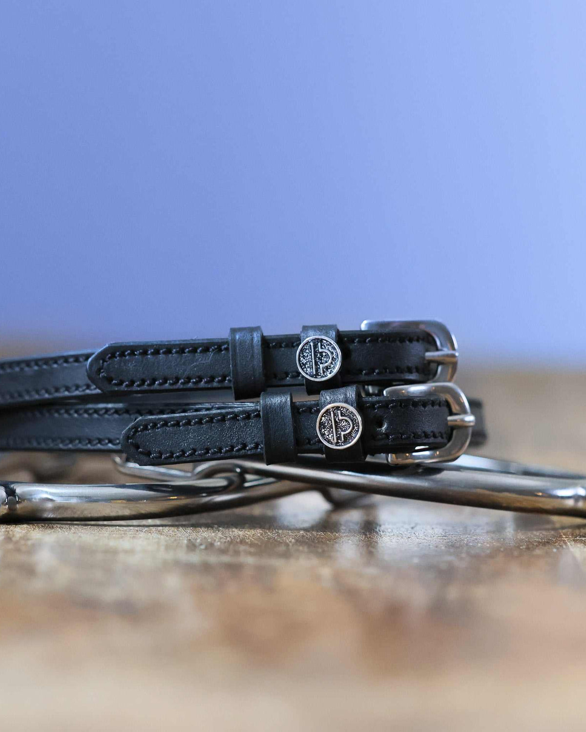 Black leather Libra zodiac spur straps coiled beside a silver spur on wood
