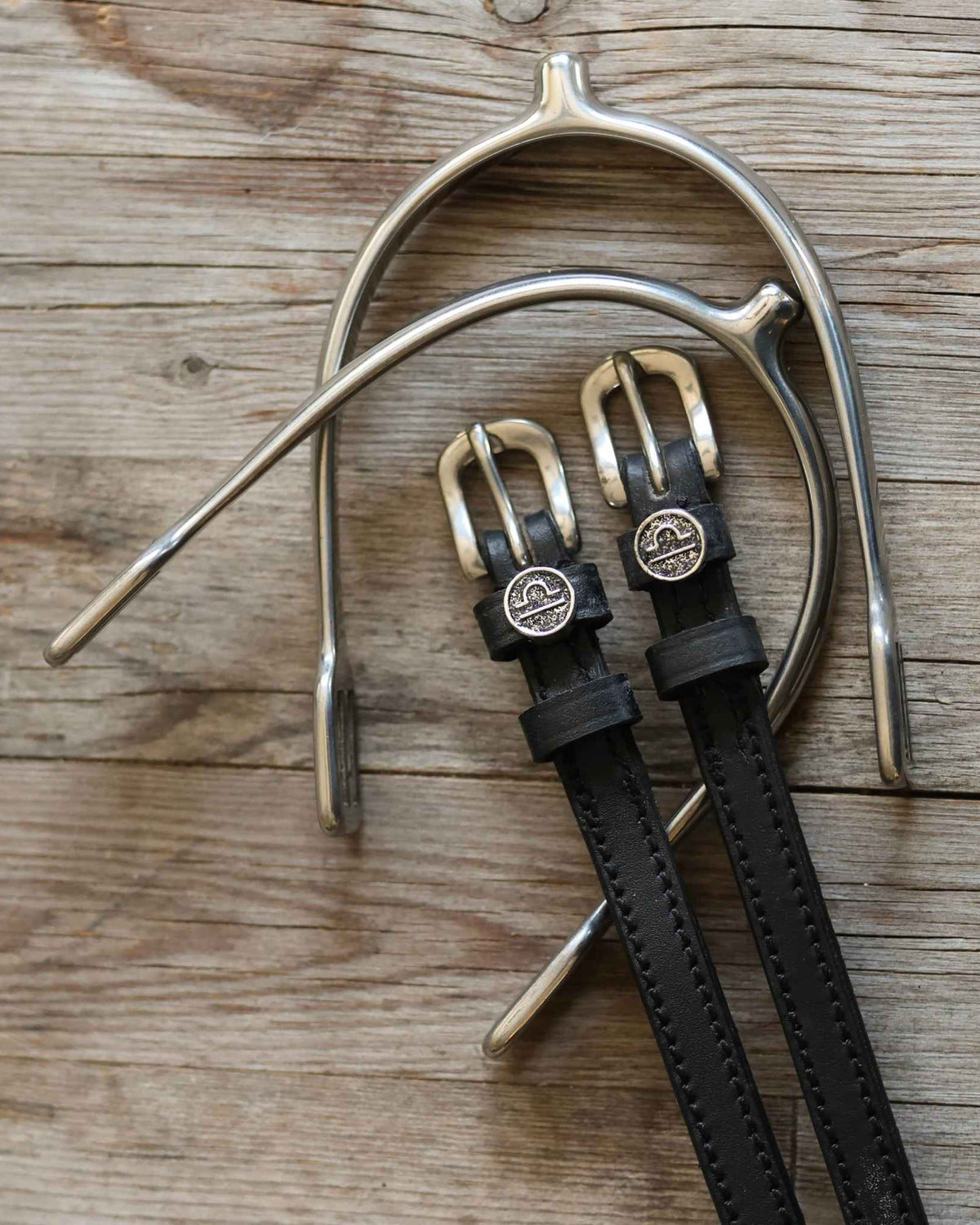Black leather Libra spur straps arranged with a silver spur on rustic wood