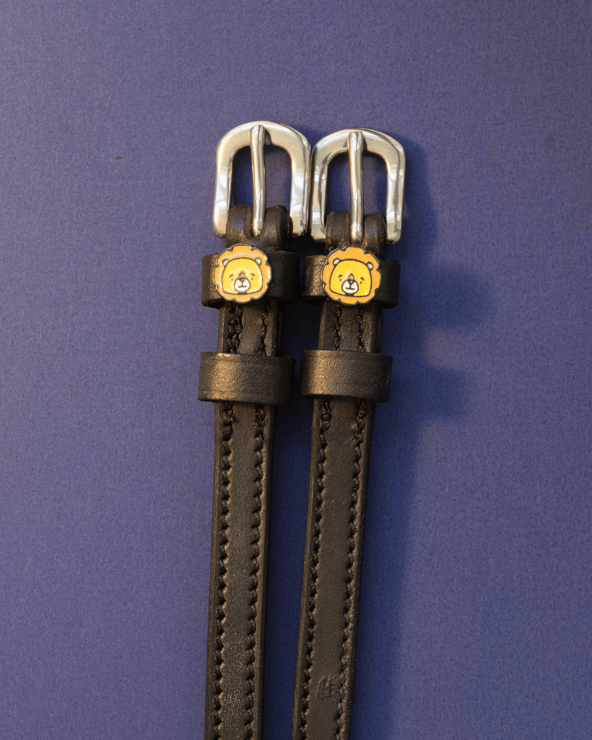 Black leather lion charm spur straps with silver buckles on a deep purple background