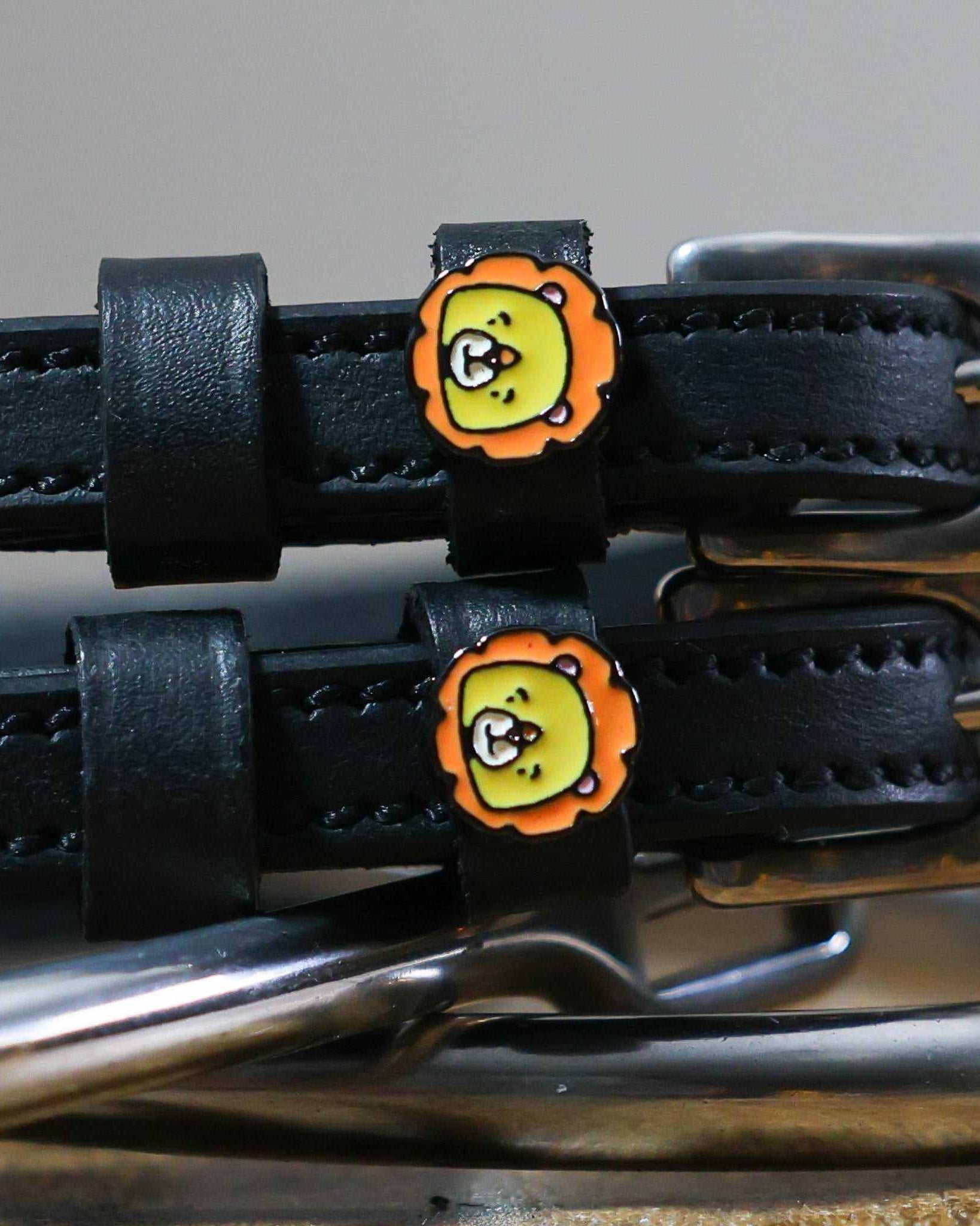 Close-up of orange-maned cartoon lion charms on black leather spur strap keepers
