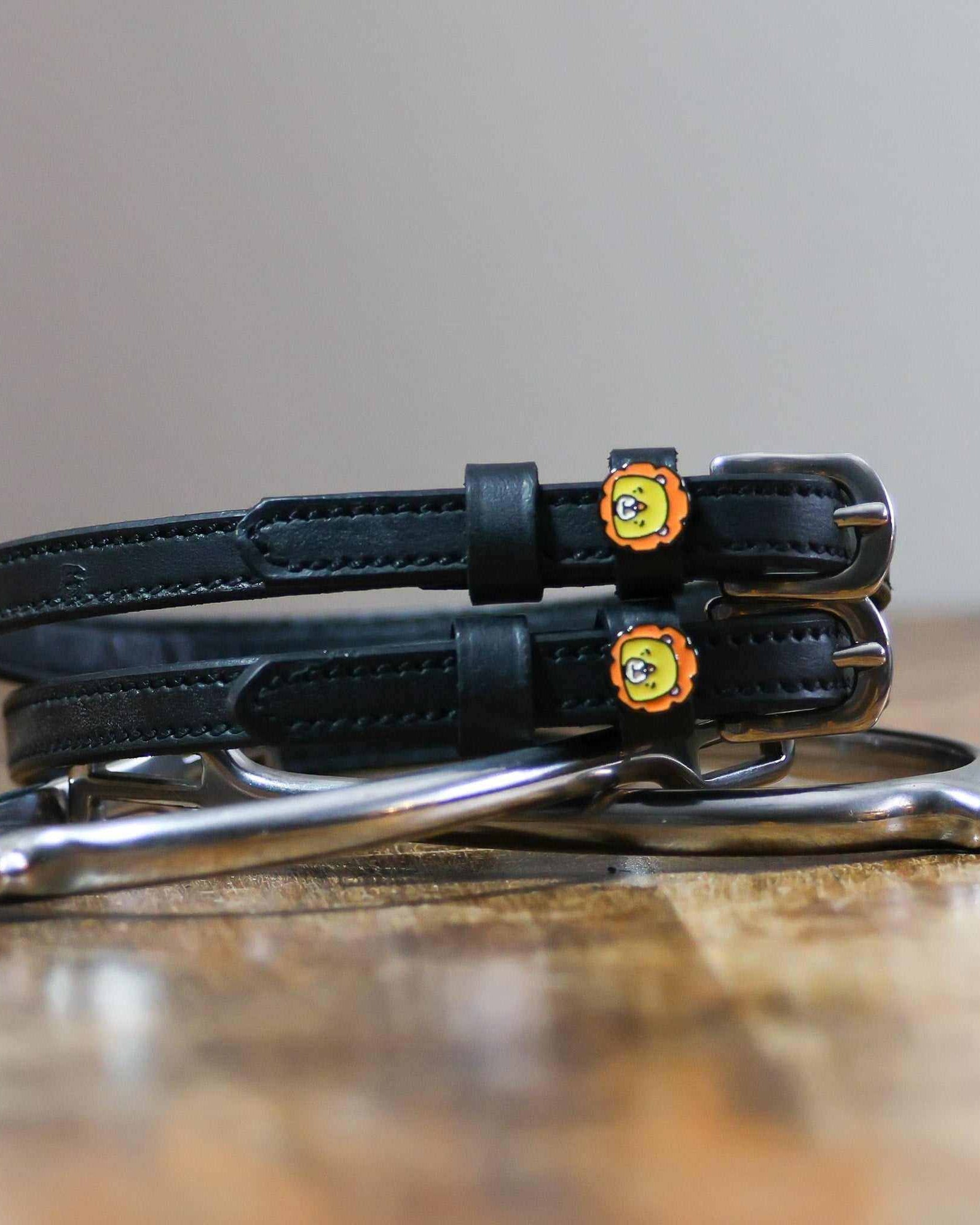 Black lion charm spur straps coiled beside a silver spur on a rustic wood surface
