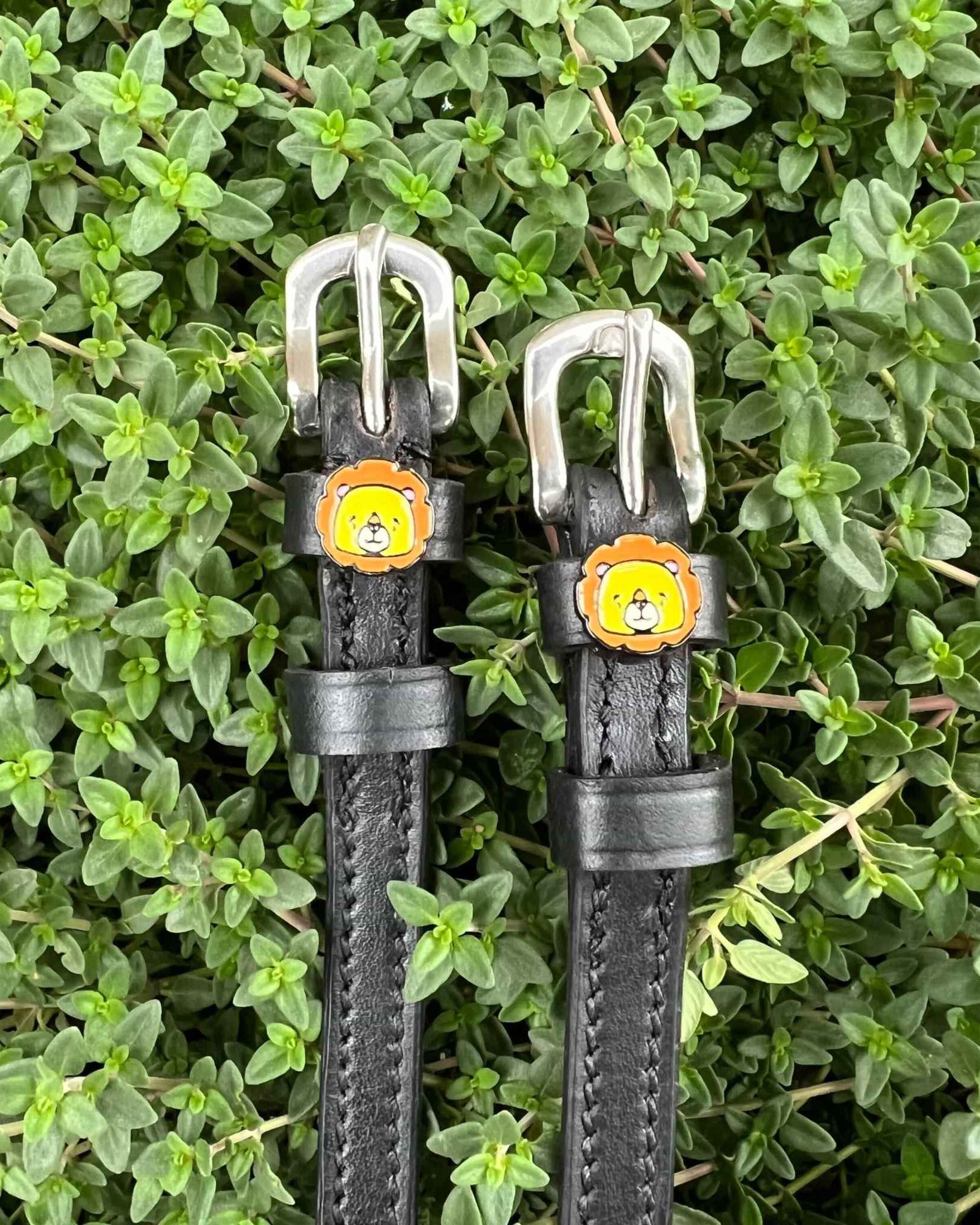 Black leather ManeJane lion spur straps set against green garden foliage