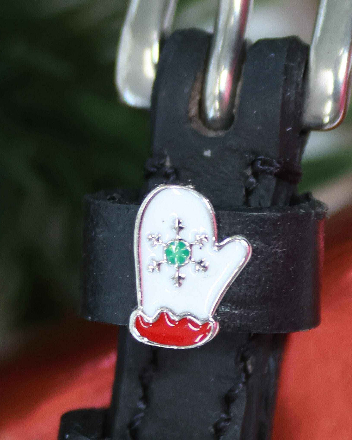 Extreme close-up of a white mitten charm with green snowflake on a black leather spur strap