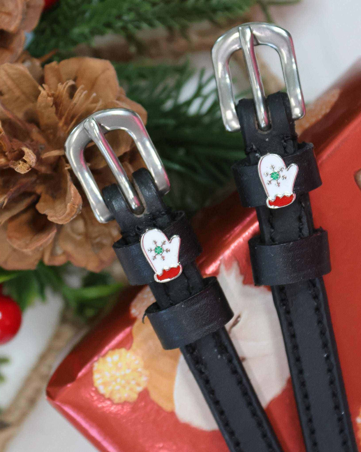 Black leather ManeJane mitten spur straps with silver buckles beside a red holiday gift