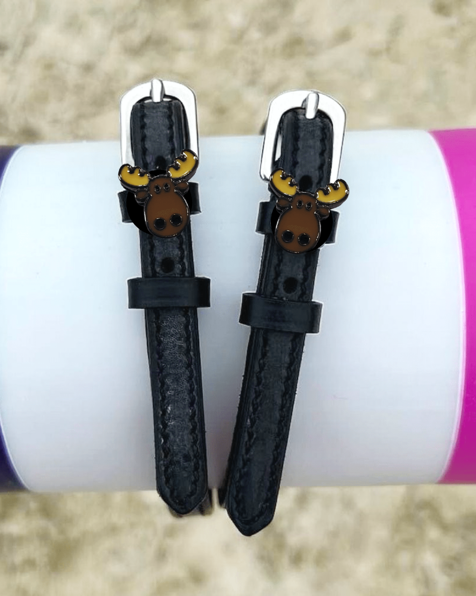 ManeJane moose spur straps draped over a colorful jump pole in a sand arena
