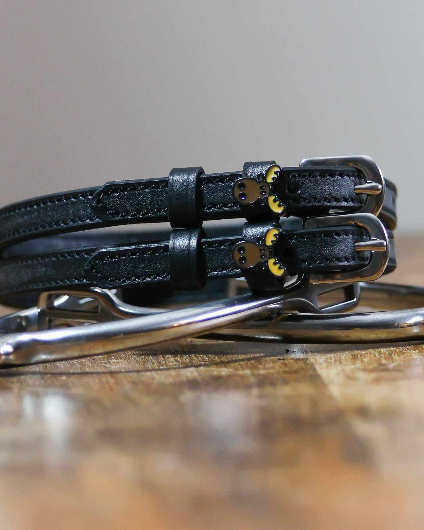 Black moose head spur straps stacked on a silver spur on wood, close-up
