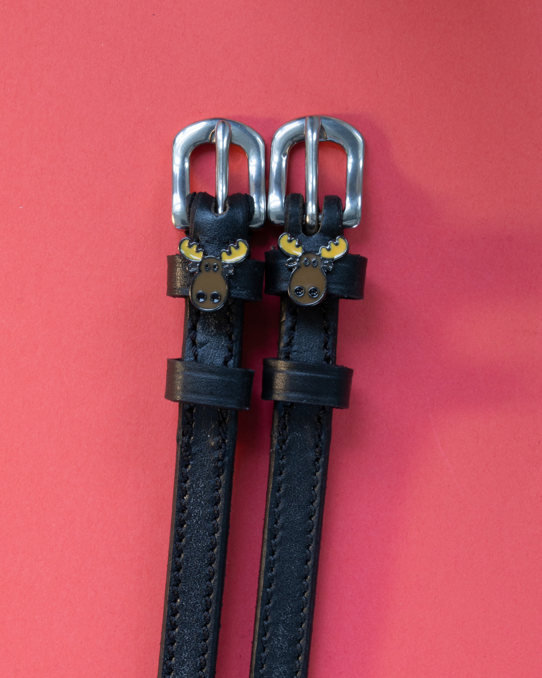 Pair of black leather moose head spur straps flat-laid on a coral background