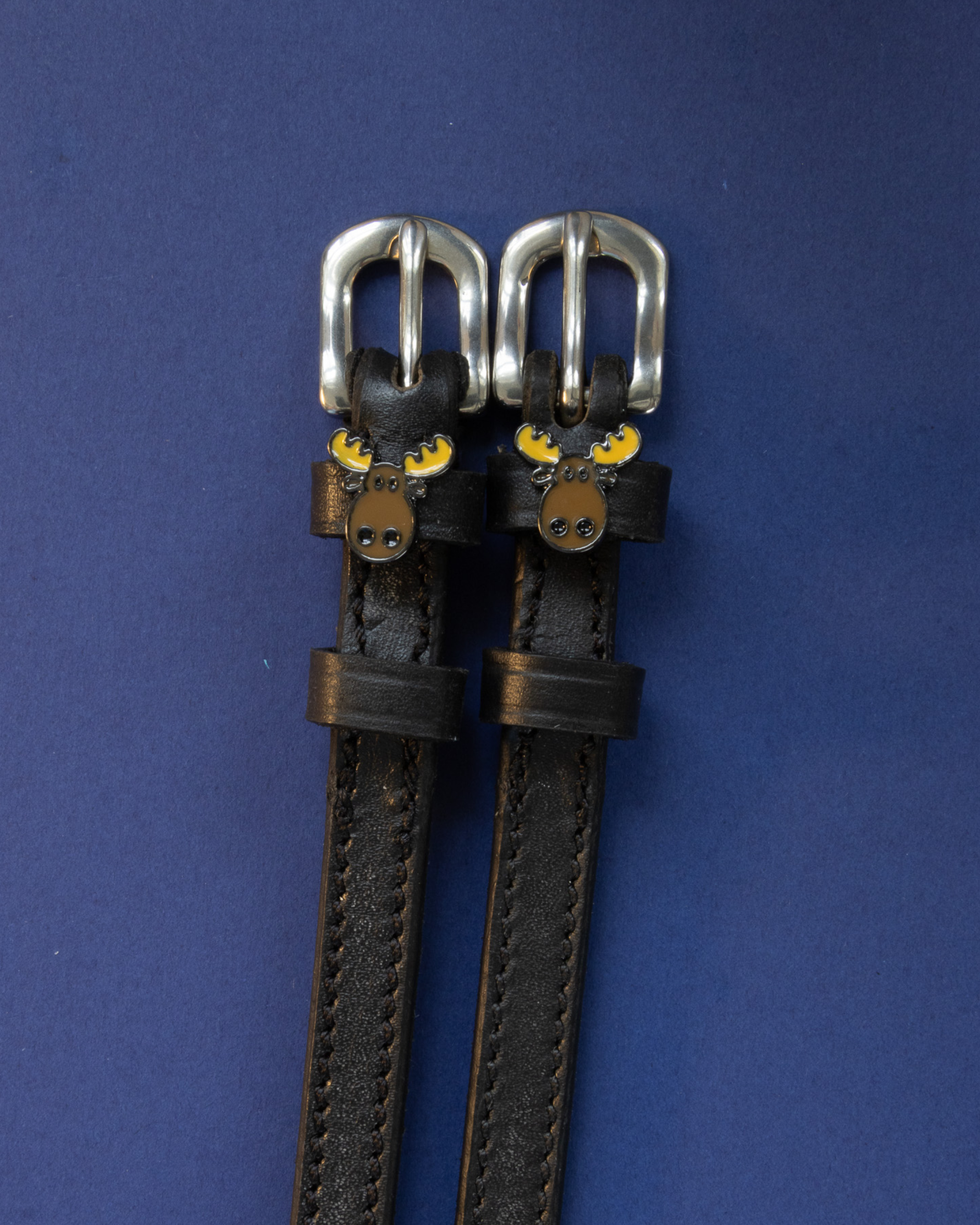 Dark brown leather moose spur straps flat-laid on a navy blue background