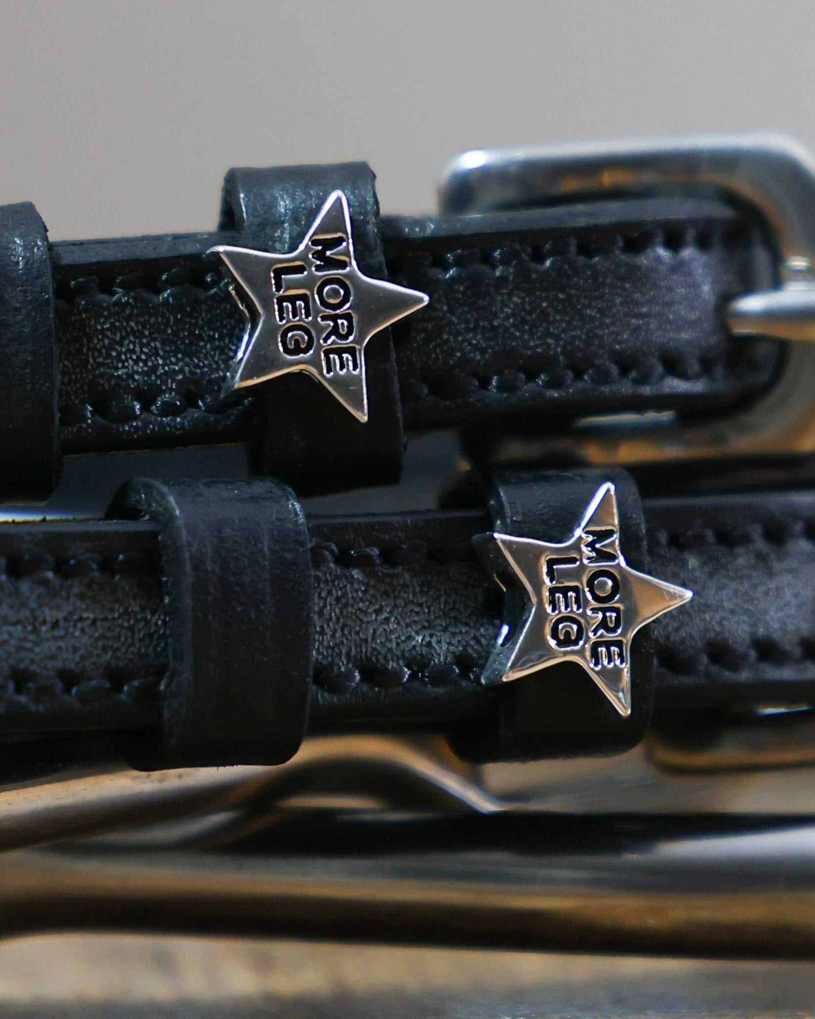 Close-up of silver MORE LEG star charms on black leather spur strap keepers