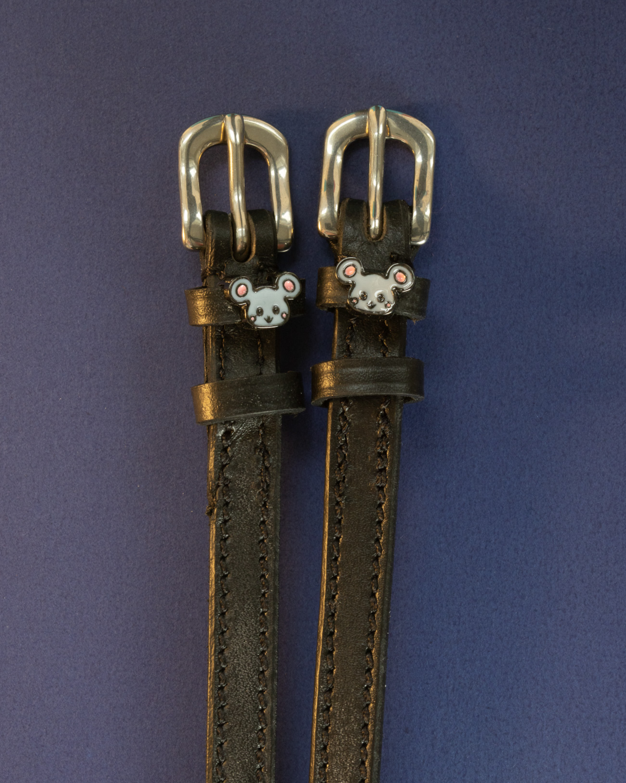 Black leather ManeJane Mouse spur straps with silver buckles on a navy background
