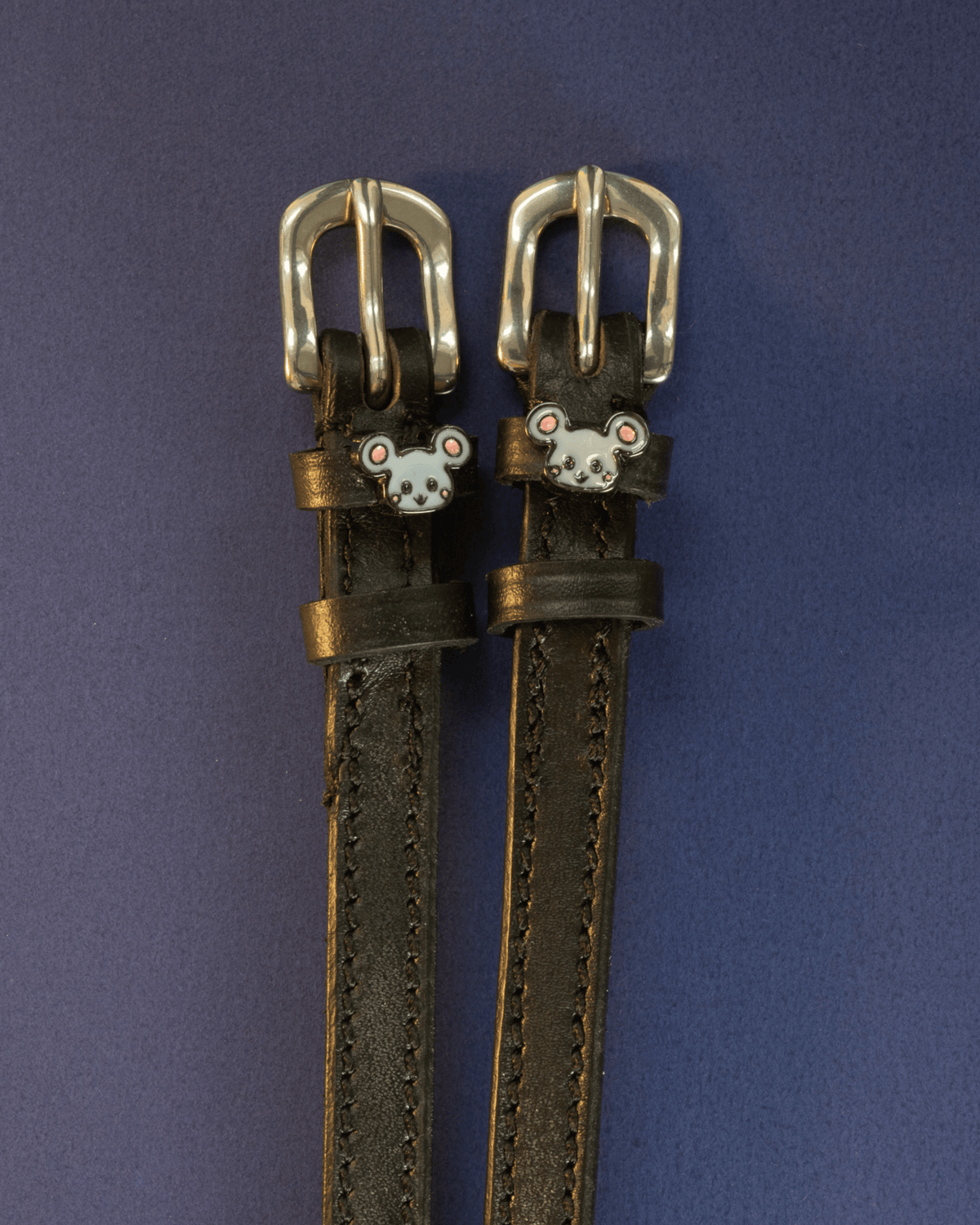 Black leather ManeJane Mouse spur straps with silver buckles on a navy background