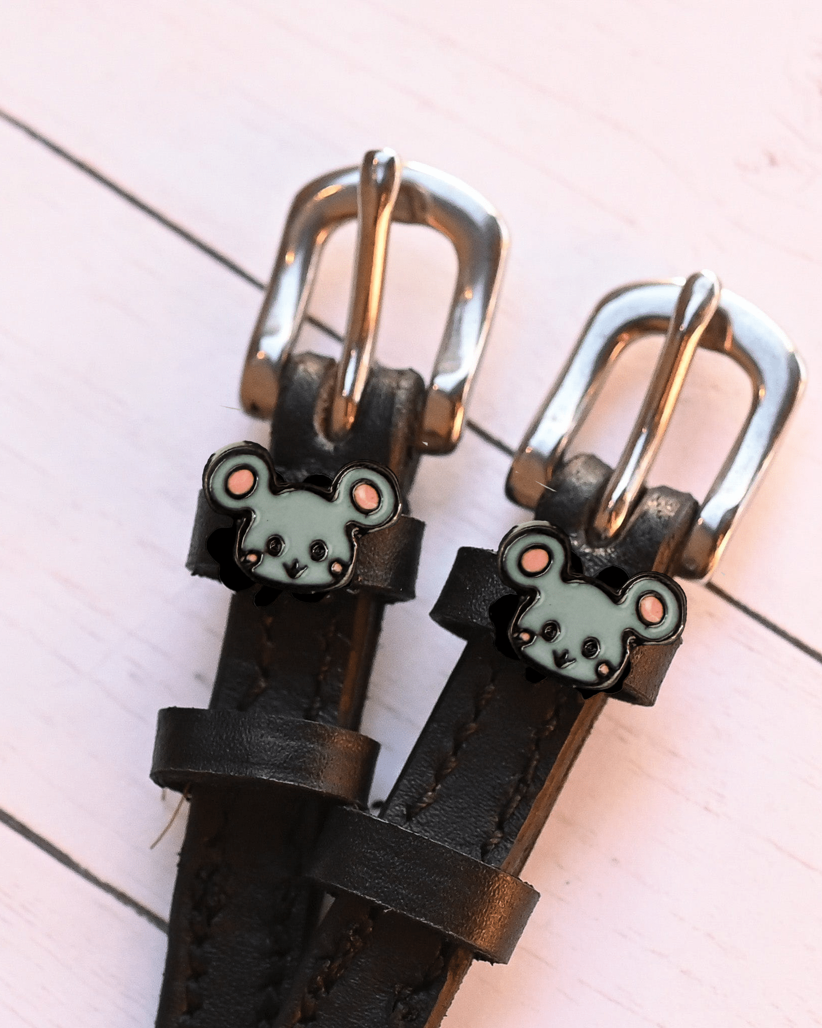 Close-up of grey mouse charms on black spur straps with silver buckles on pink planks