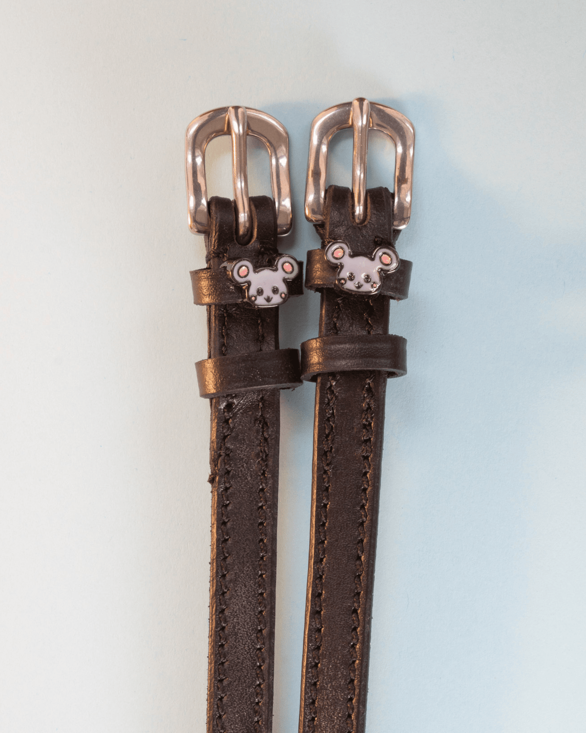 Dark brown Mouse spur straps with rose gold buckles and grey mouse charms on pale blue