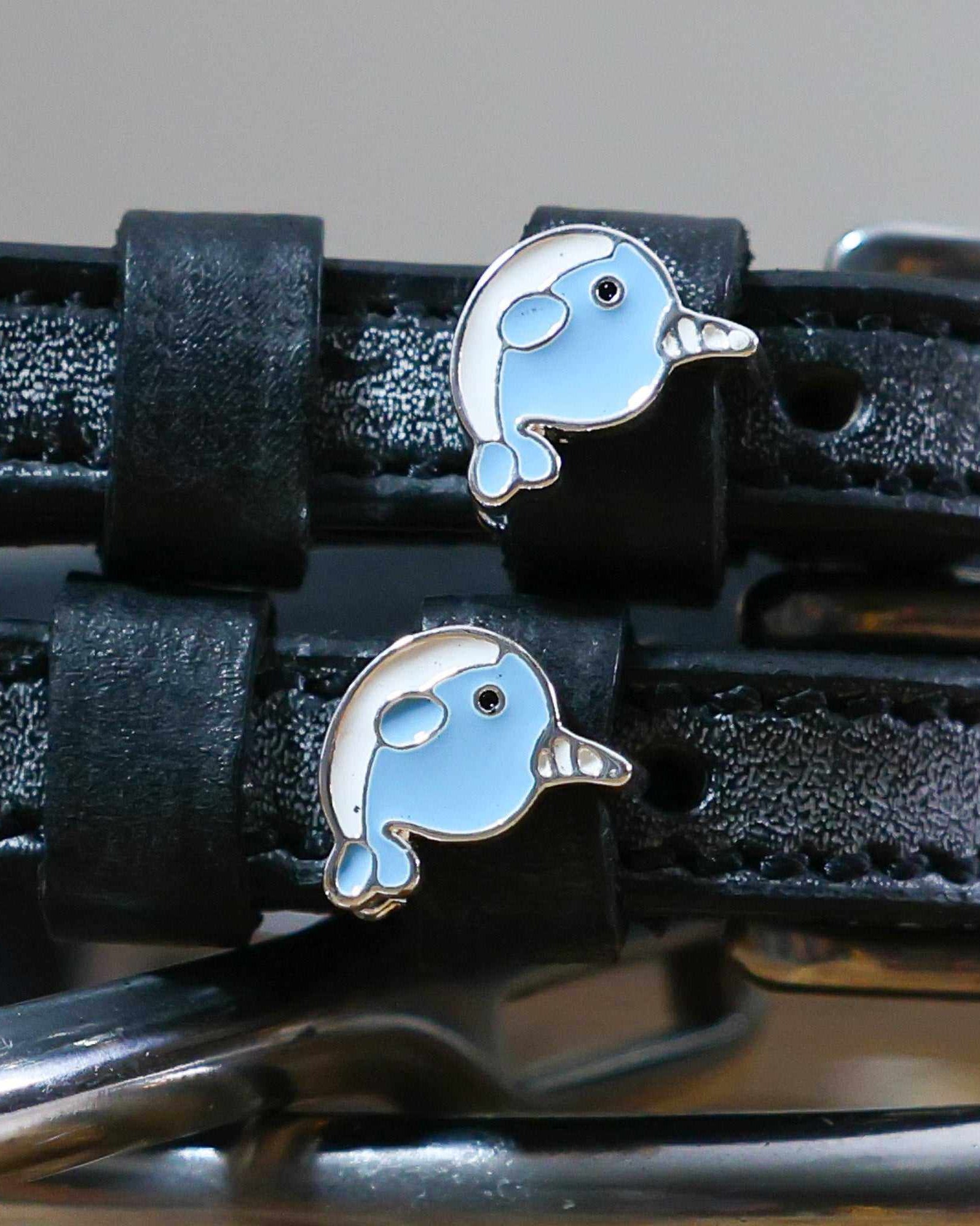Close-up of two blue enamel narwhal charms on black leather ManeJane spur strap keepers