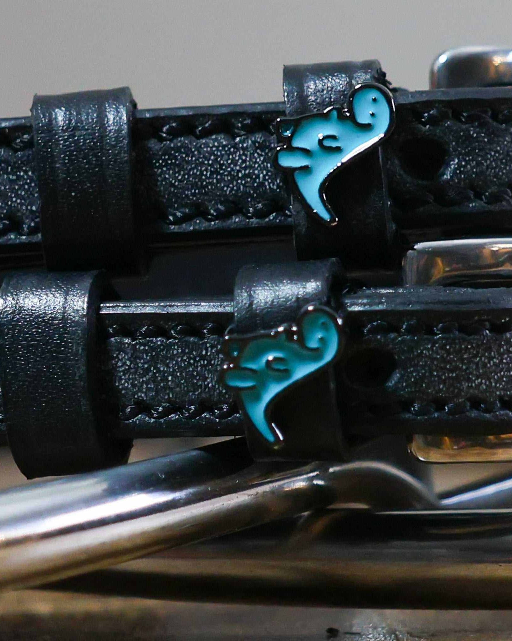 Close-up of teal dinosaur charms on black leather ManeJane spur strap keepers