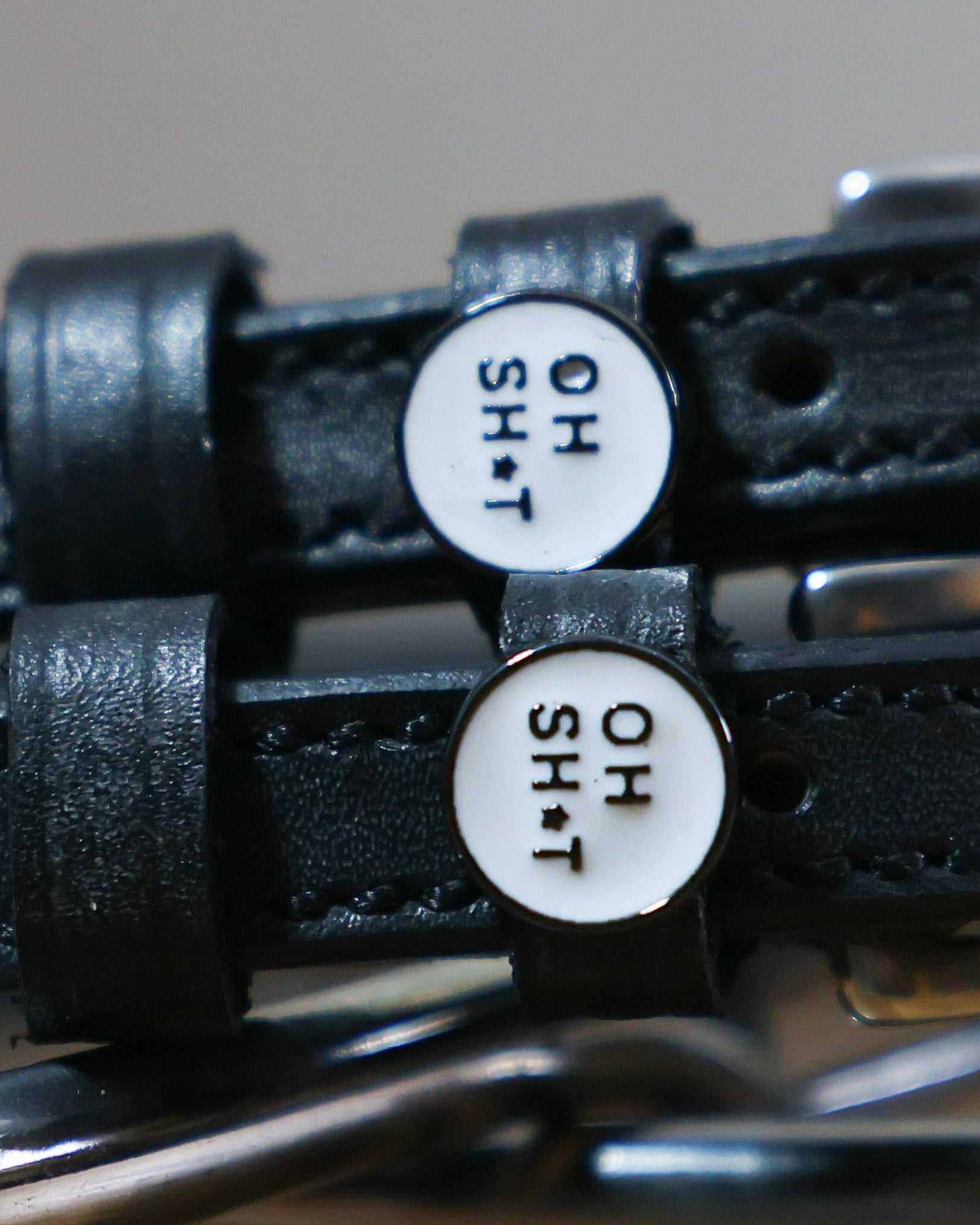Close-up of round OH SH*T text charms on black leather spur strap keepers