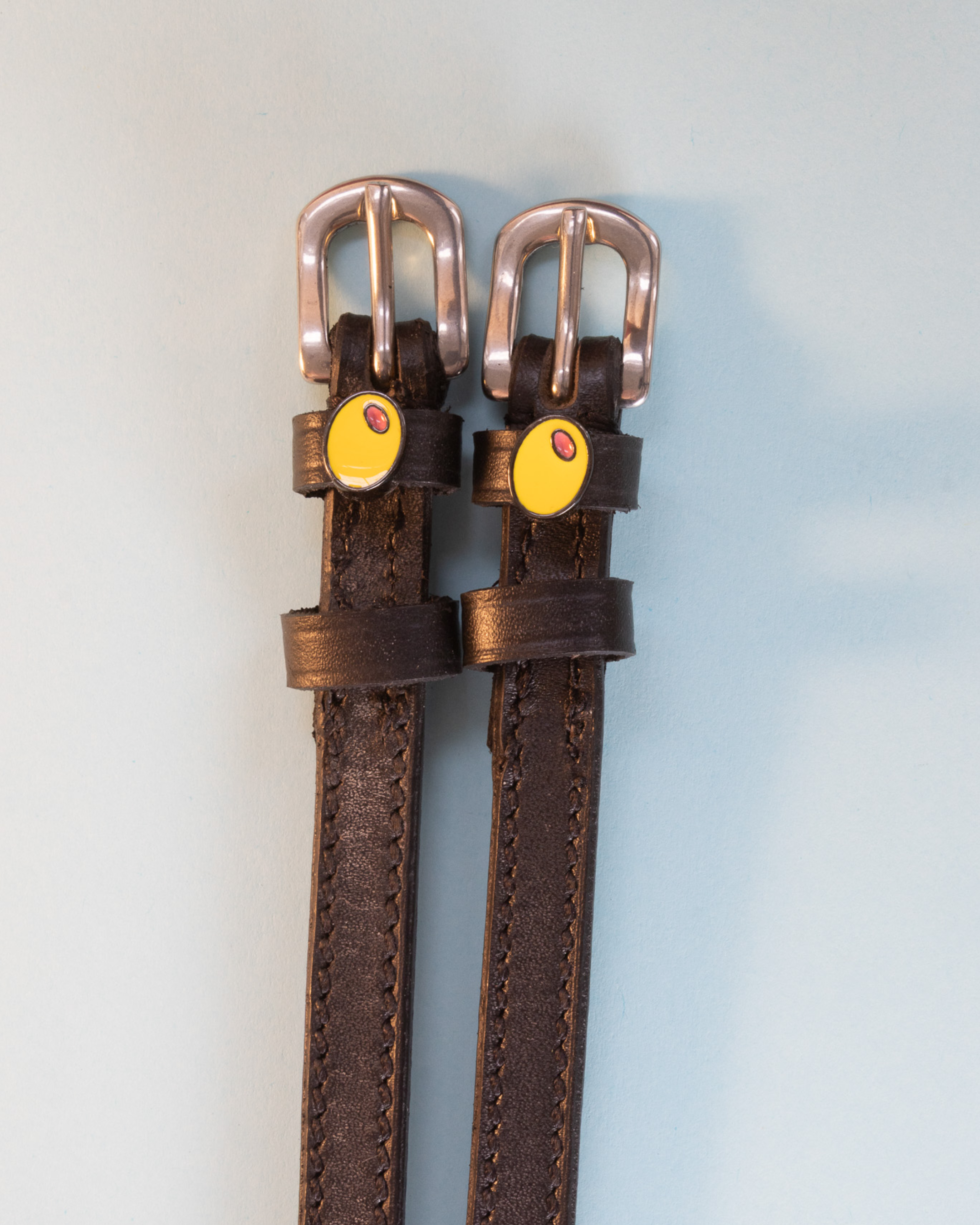 Dark brown leather olive spur straps with rose gold buckles on pale blue