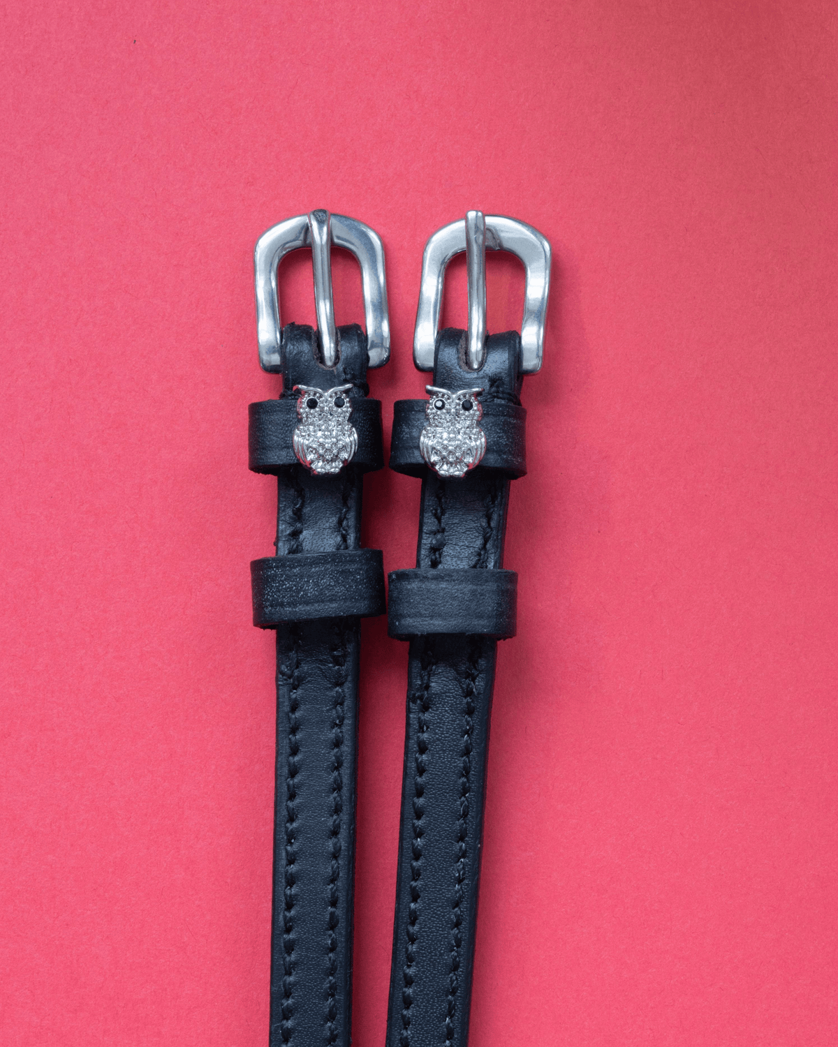 Black leather rhinestone owl spur straps with silver buckles on a red background
