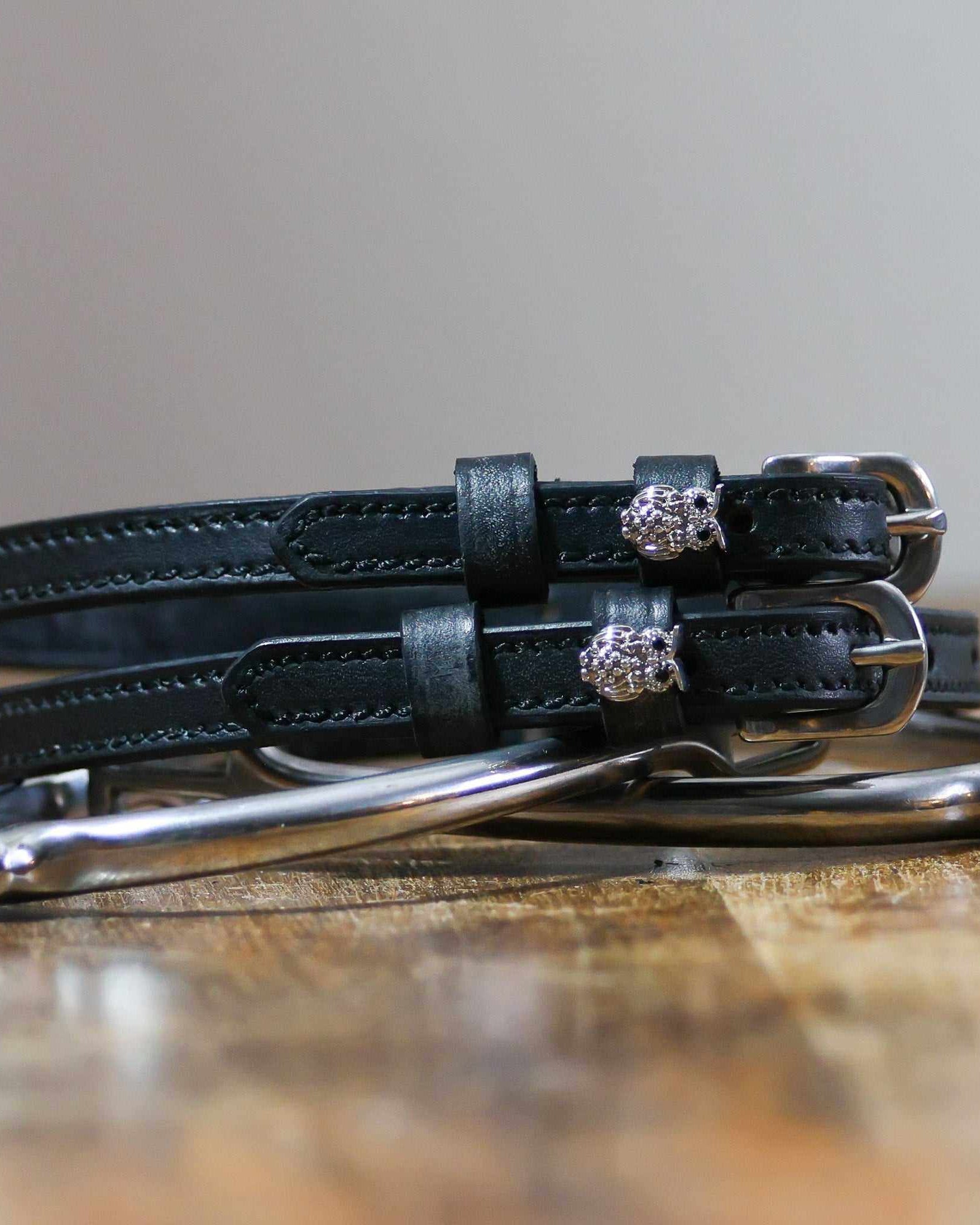Black leather owl bling spur straps coiled beside a silver spur on a wood surface