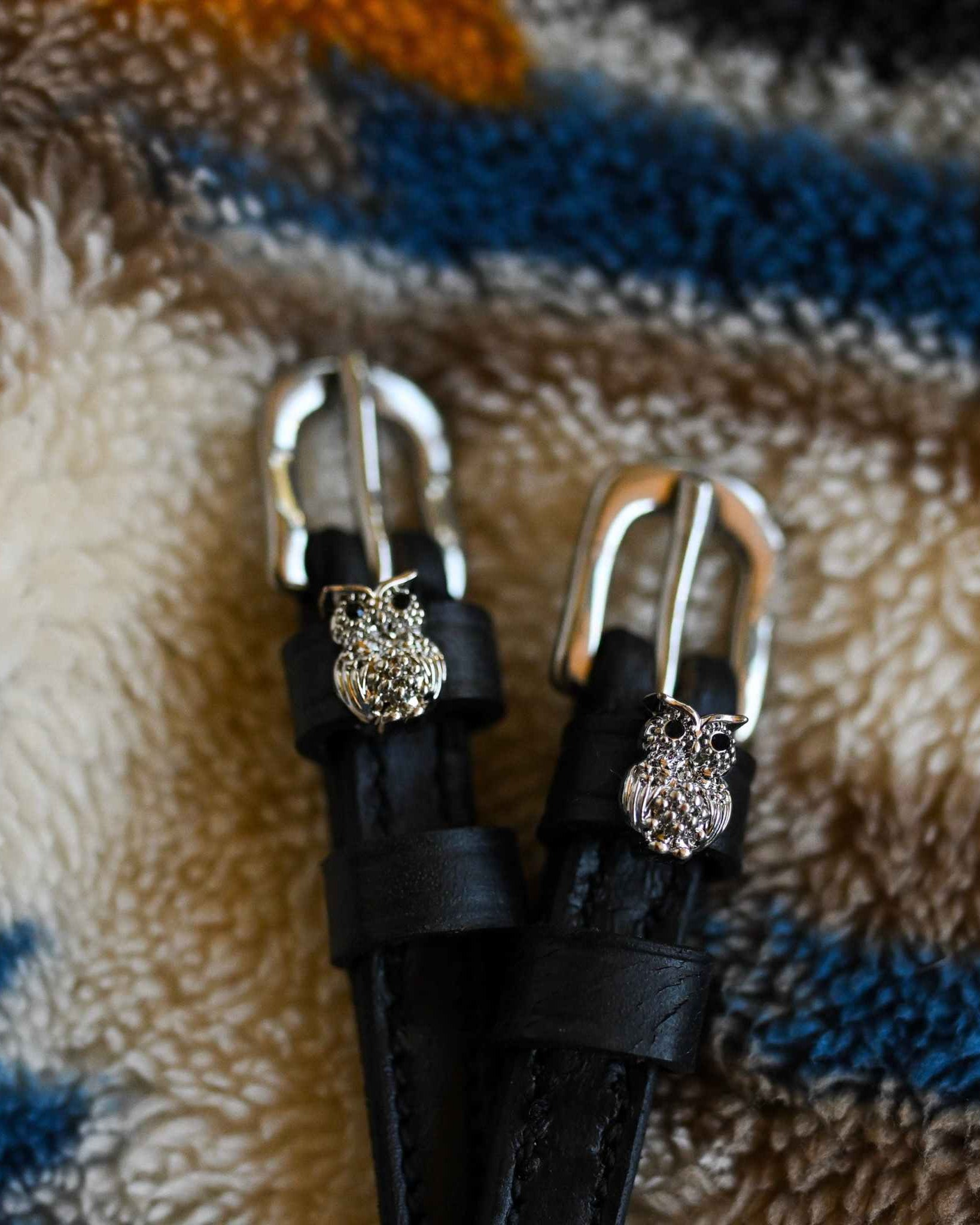 Black leather crystal owl spur straps with silver buckles laid on a cozy sherpa blanket