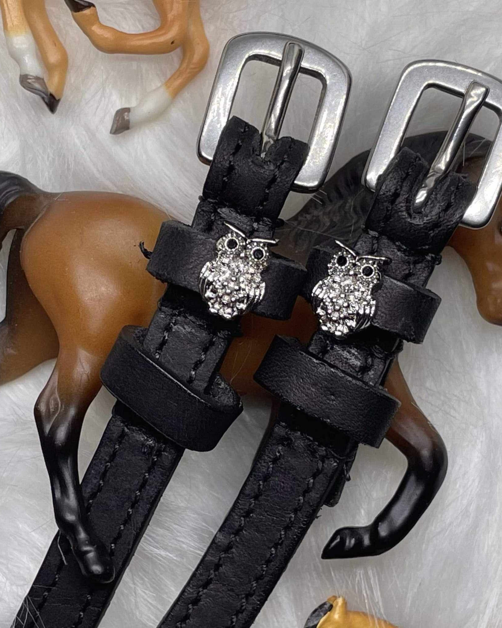 Silver crystal owl spur straps styled with toy horse figurines on white fur