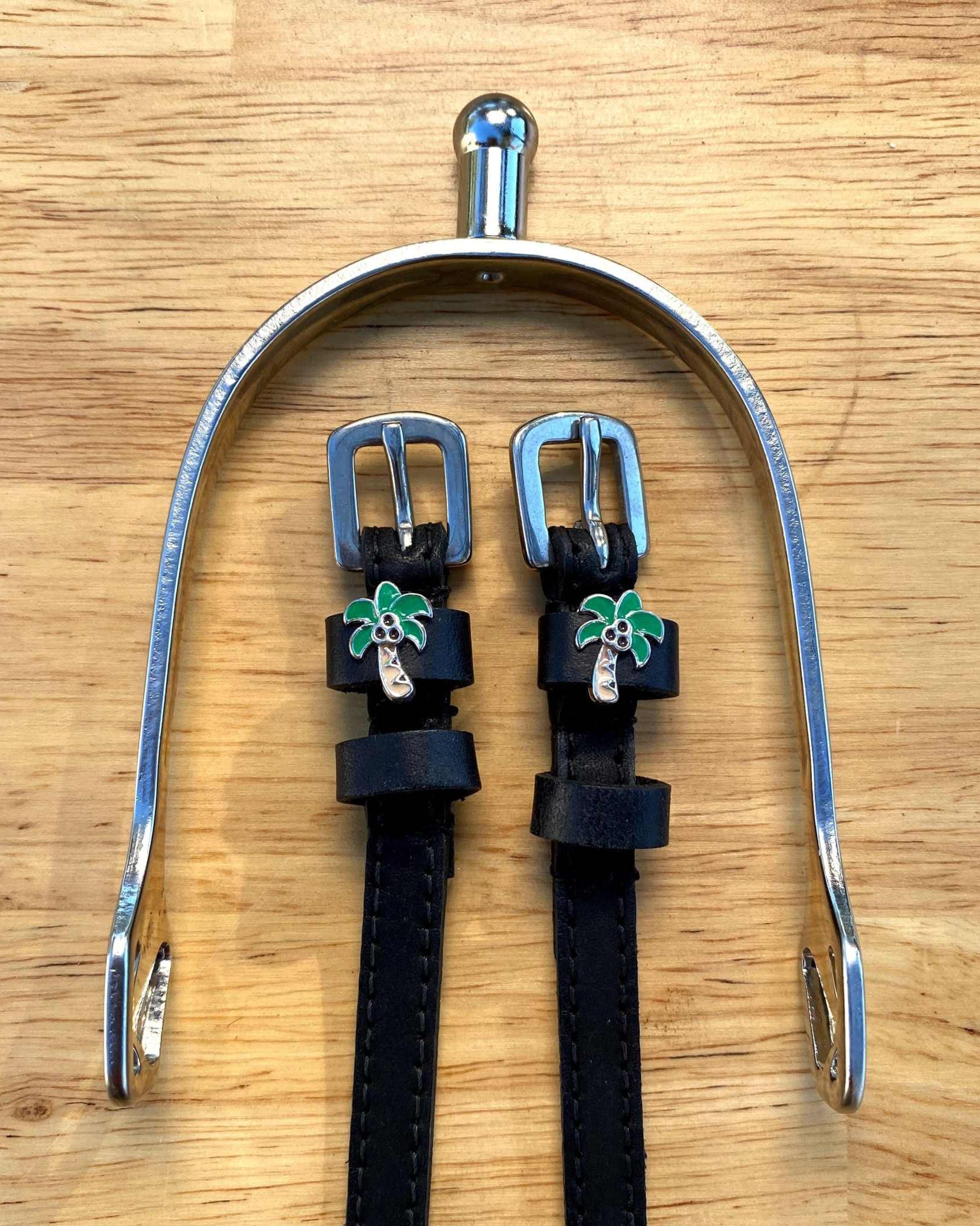 Black leather palm tree spur straps framed by a silver spur on light wood