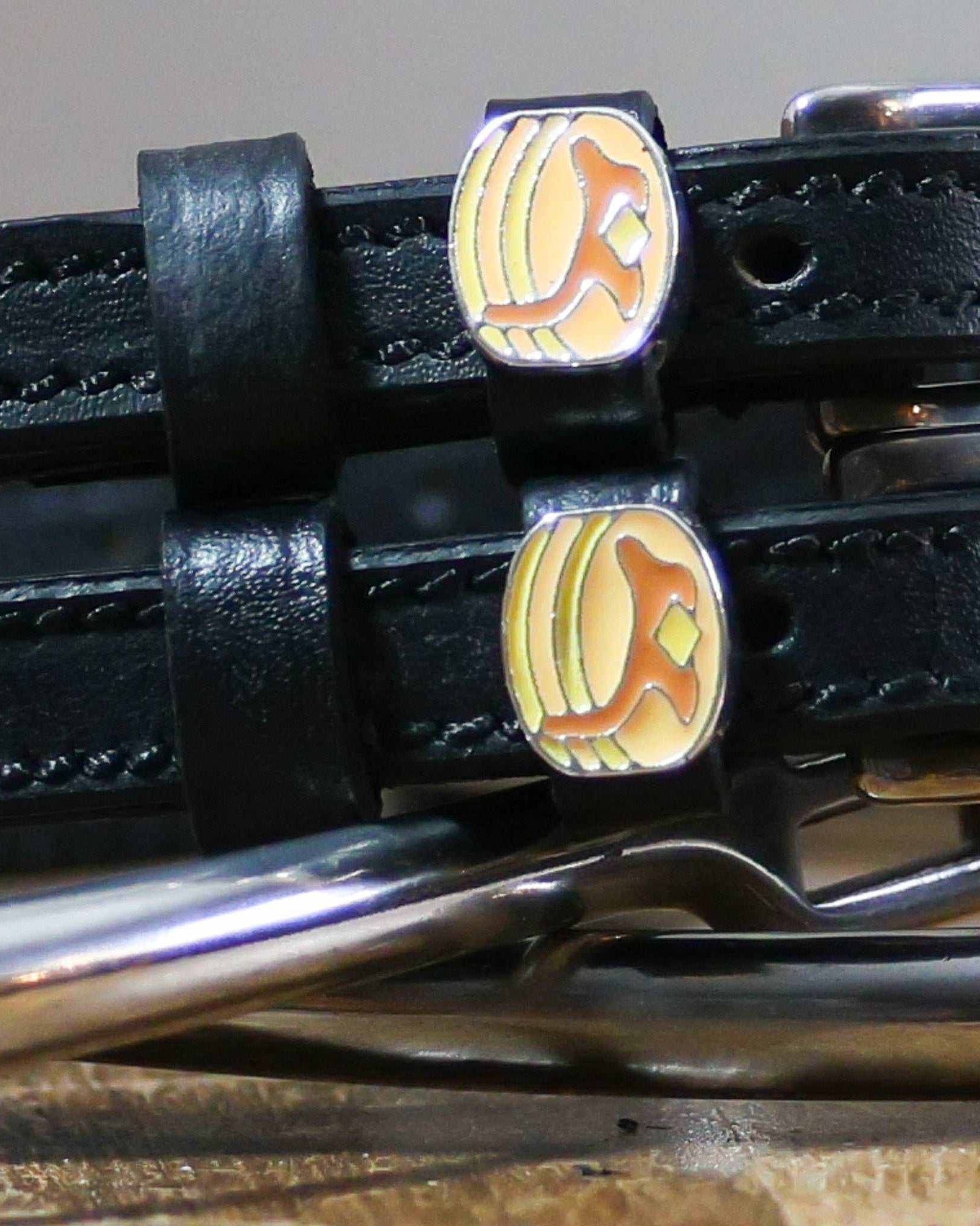 Close-up of enamel pancake stack charms on black leather ManeJane spur strap keepers