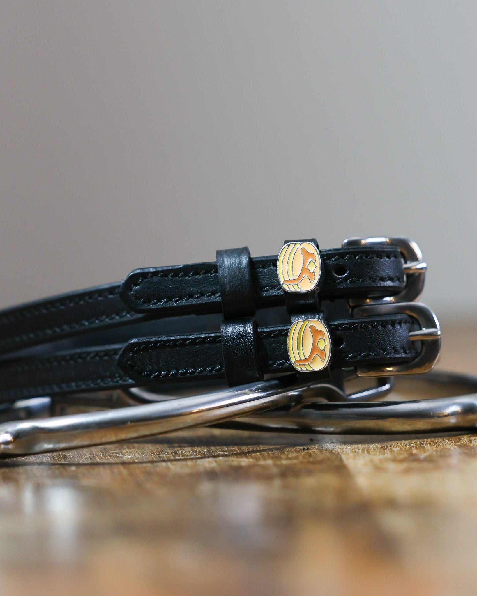 Black leather pancake spur straps coiled beside a stirrup on a wooden surface