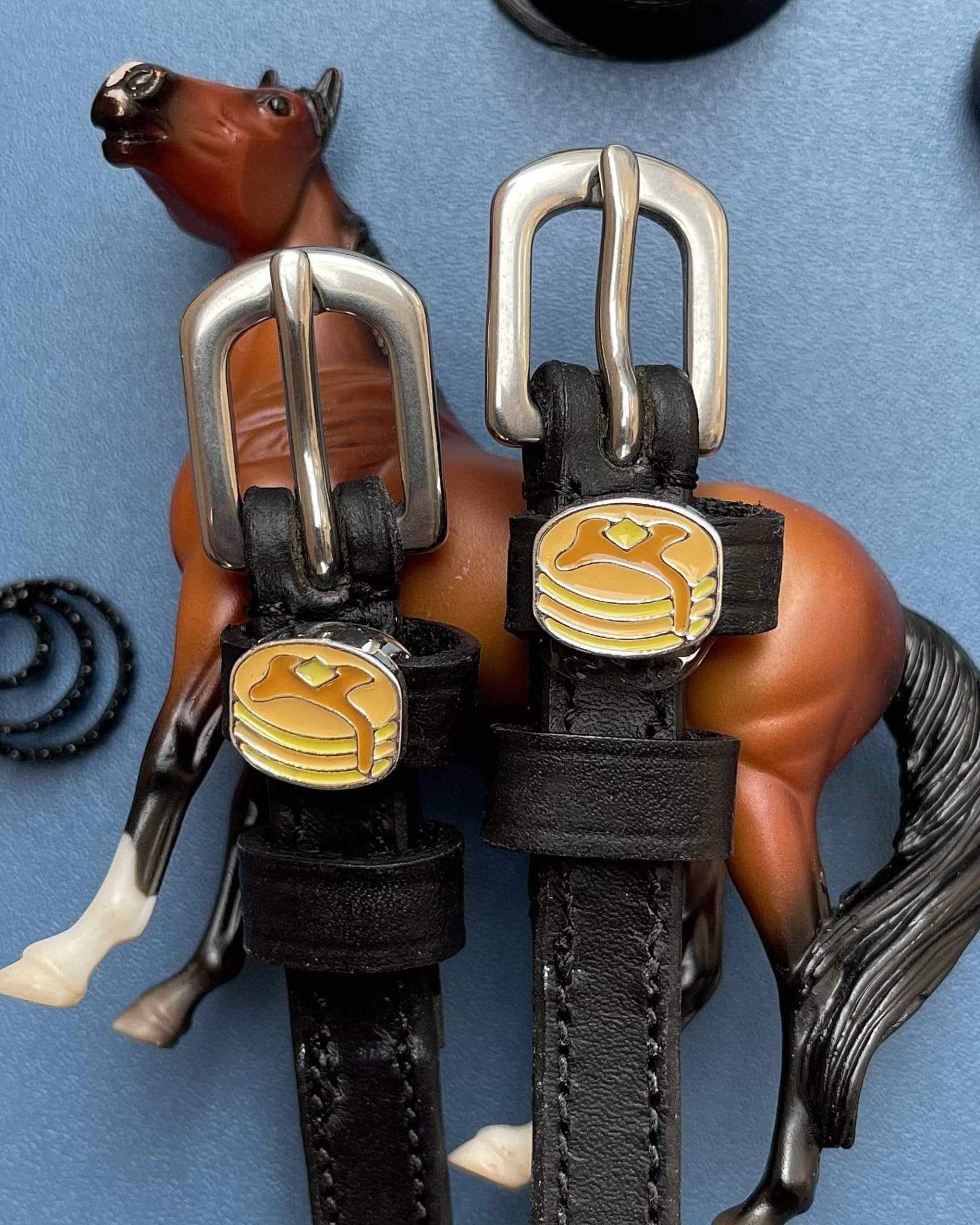 ManeJane pancake spur straps staged with a toy horse on a blue background