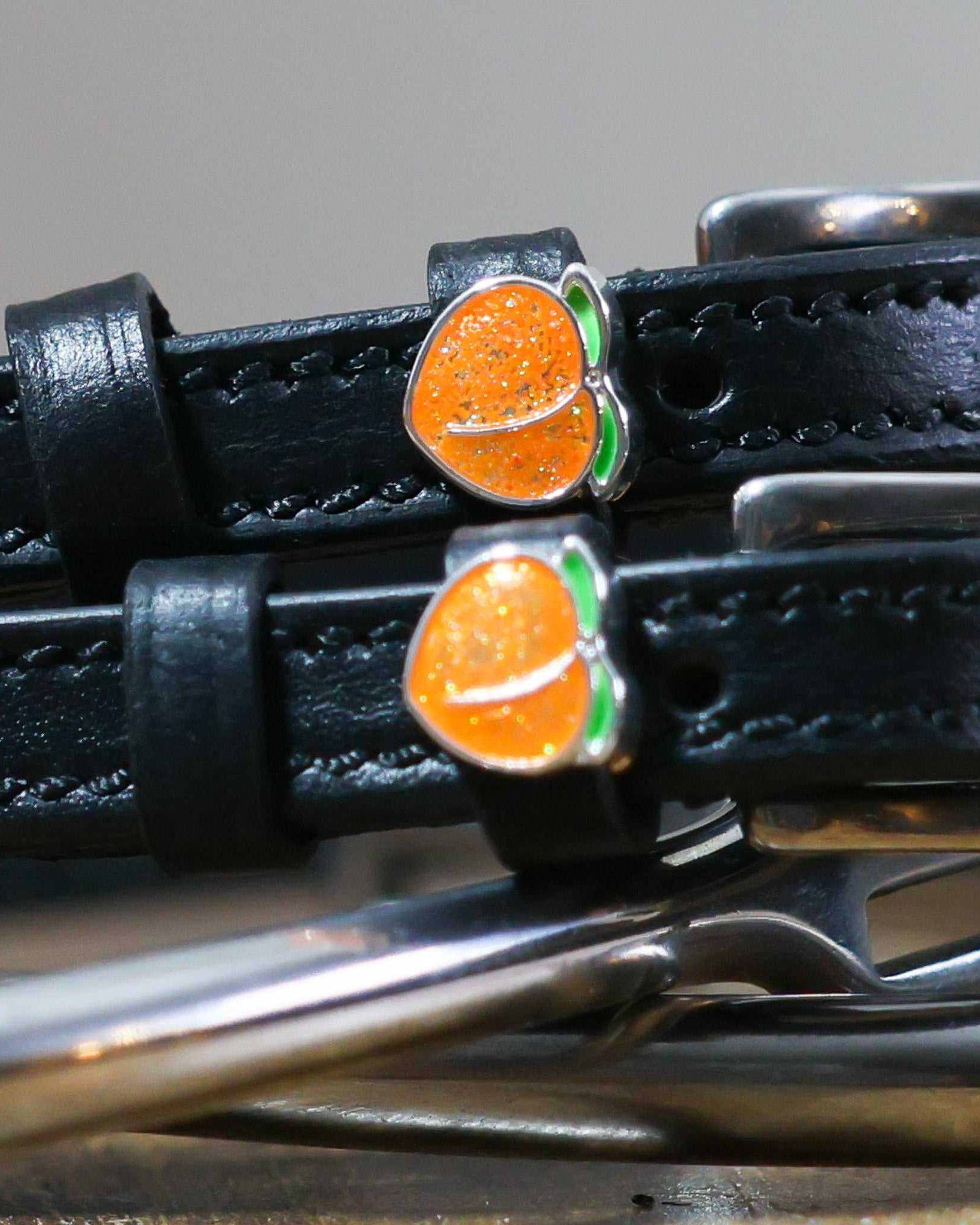 Close-up of a sparkly orange peach charm on a black leather spur strap keeper