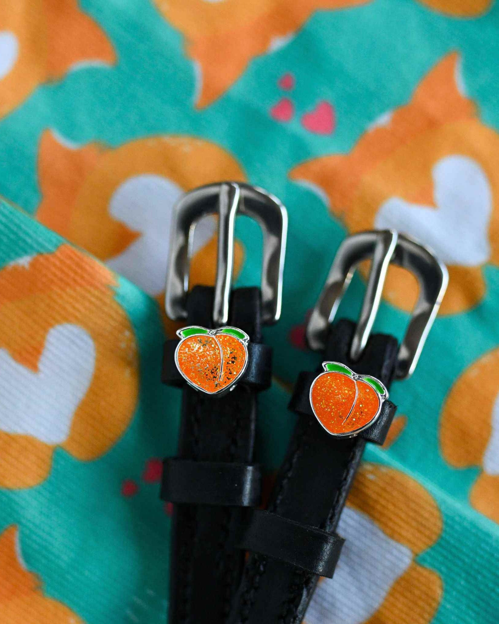 Black leather peach charm spur straps on a teal patterned fabric