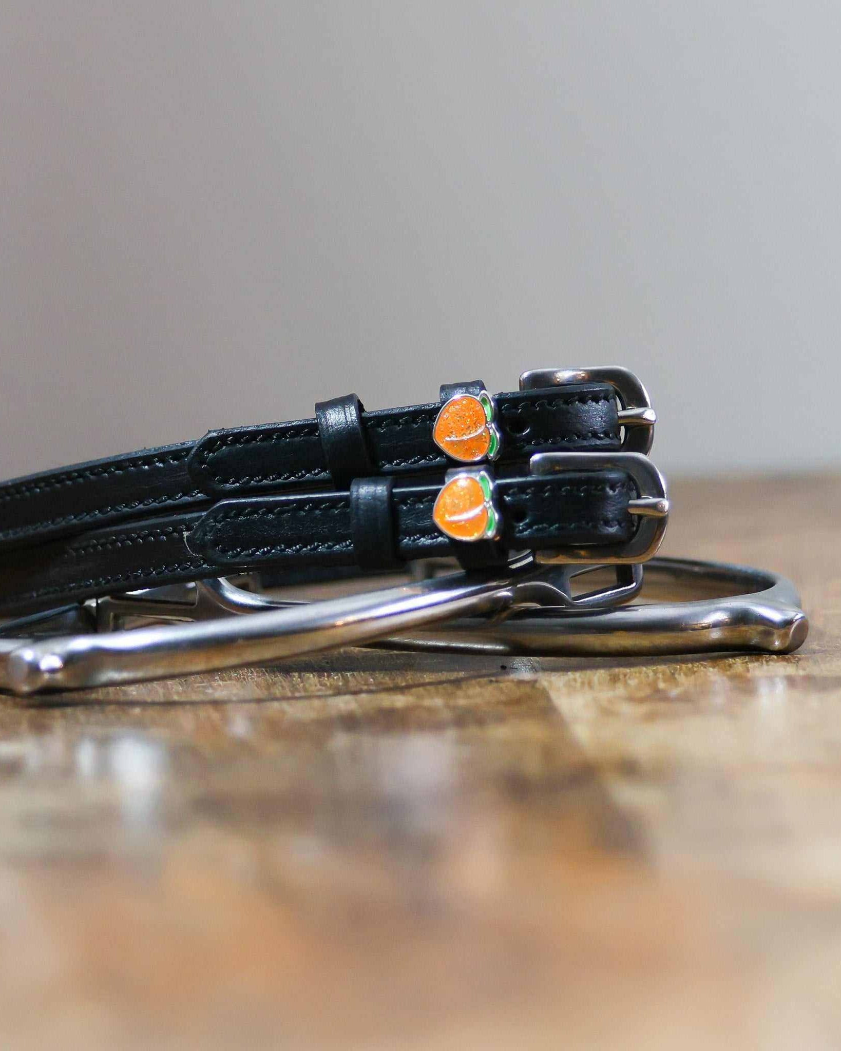 Black leather peach spur straps coiled beside a silver spur on wood