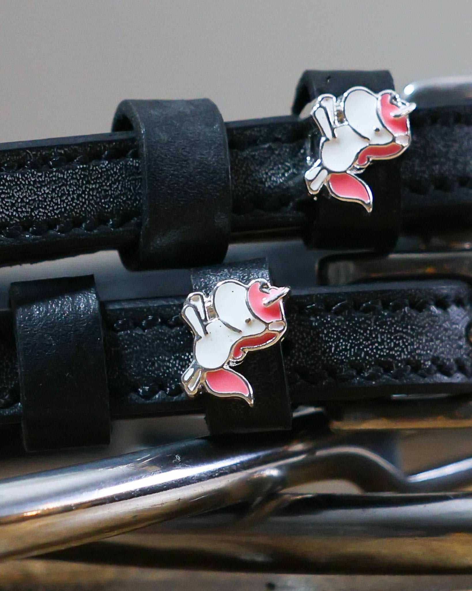 Close-up of white-and-pink unicorn charms on black leather spur strap keepers