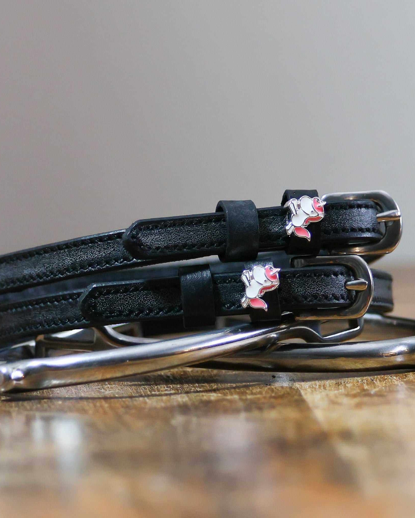Phat unicorn spur straps coiled on a silver stirrup on a wooden table