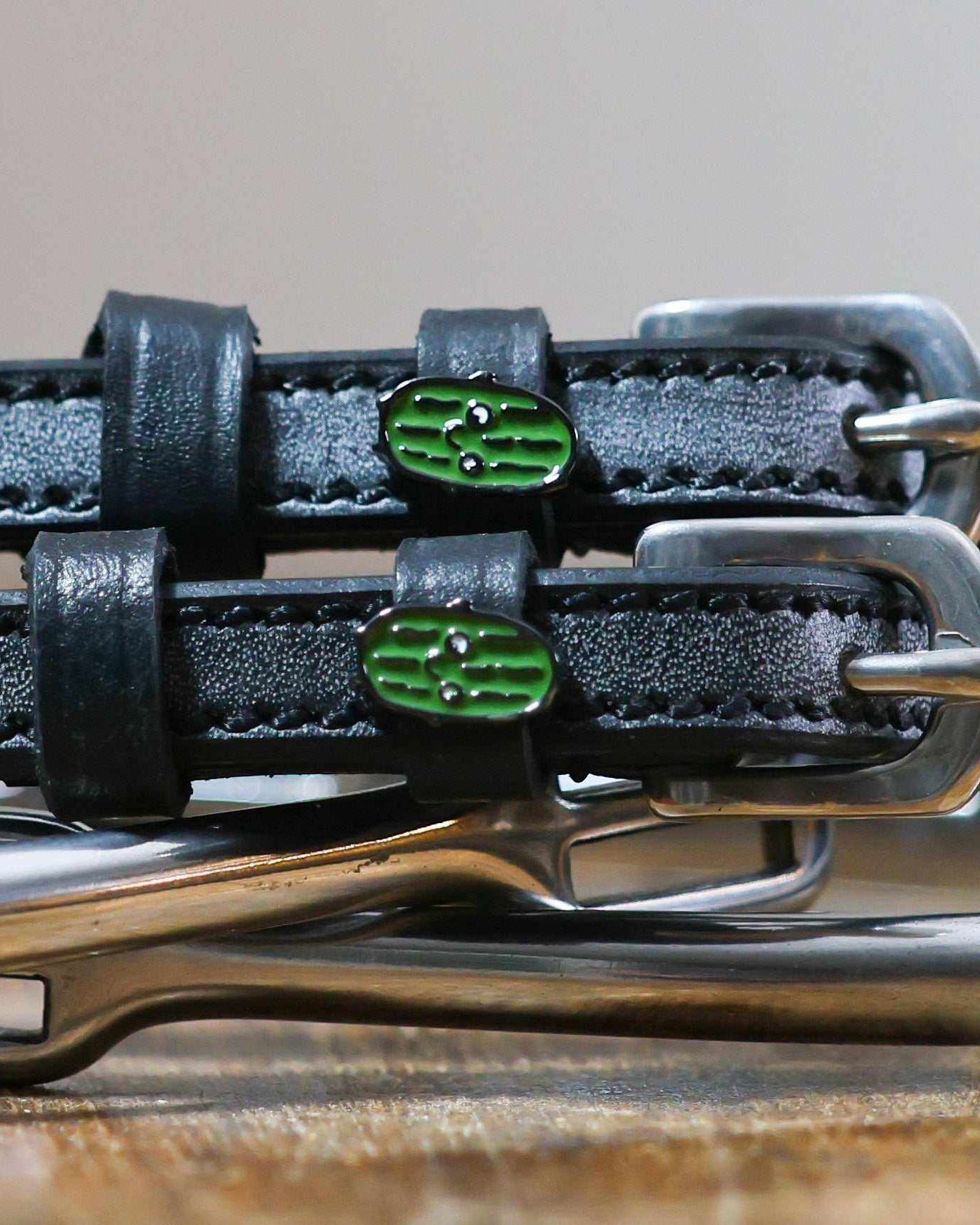 Close-up of smiling green pickle enamel charms on black leather spur strap keepers