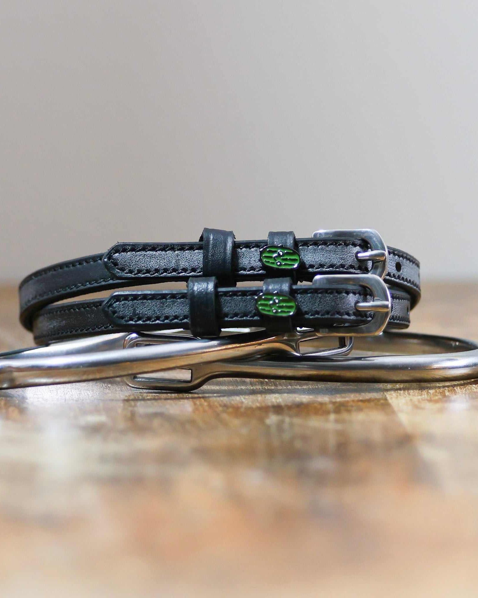 Black leather pickle spur straps coiled beside a silver spur on a wooden surface