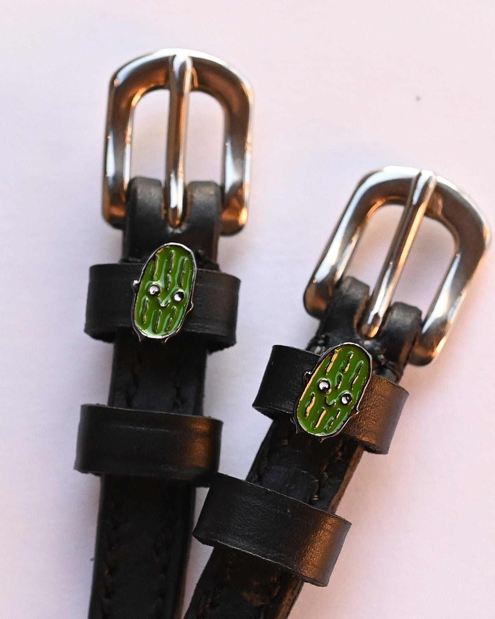 Close-up of two smiling pickle charms on black leather ManeJane spur straps over pink