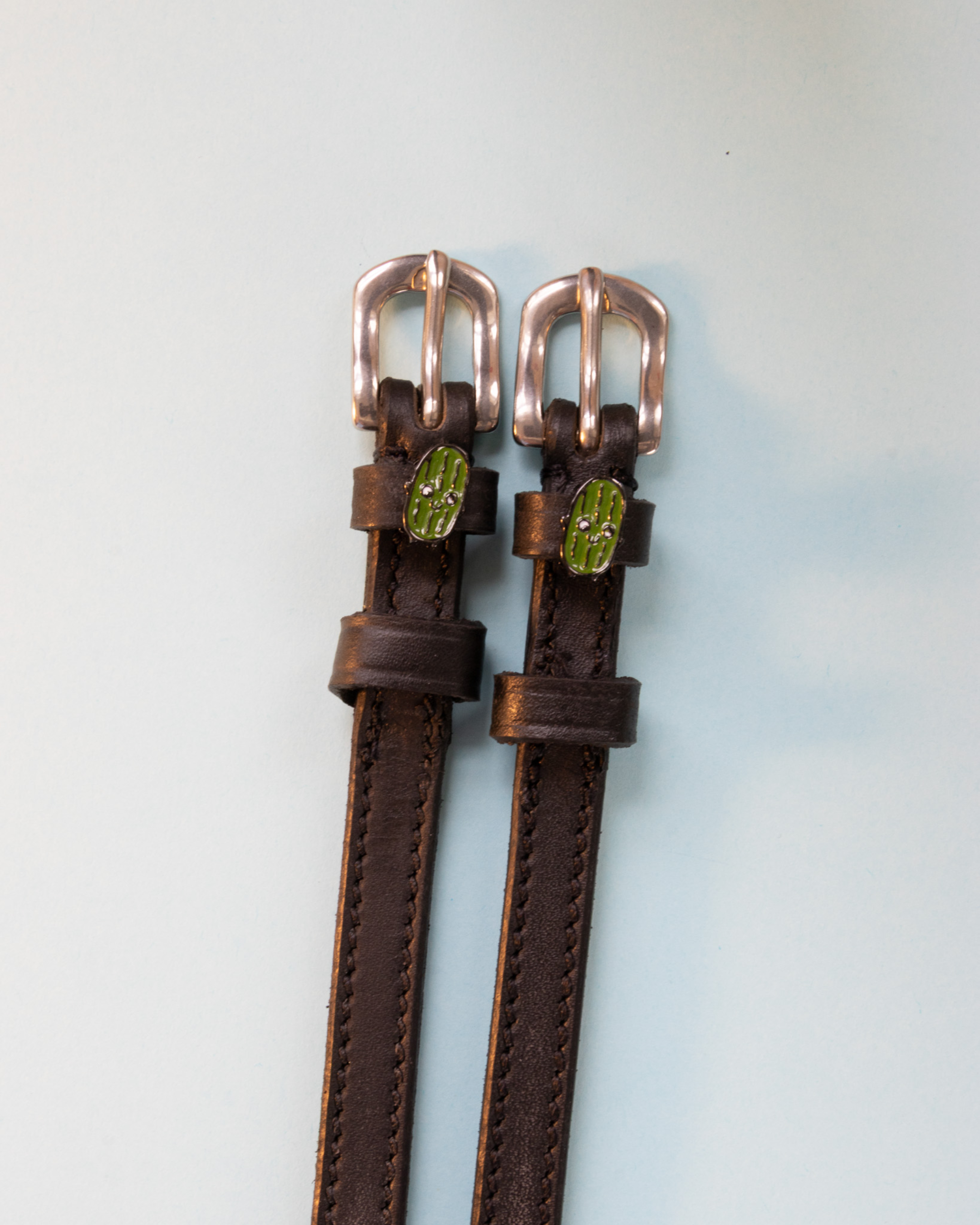 Brown leather pickle spur straps with rose gold buckles on a pale blue background