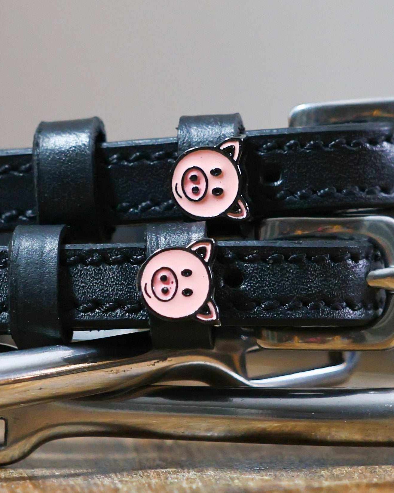 Close-up of pink pig-face charms on black leather spur strap keepers