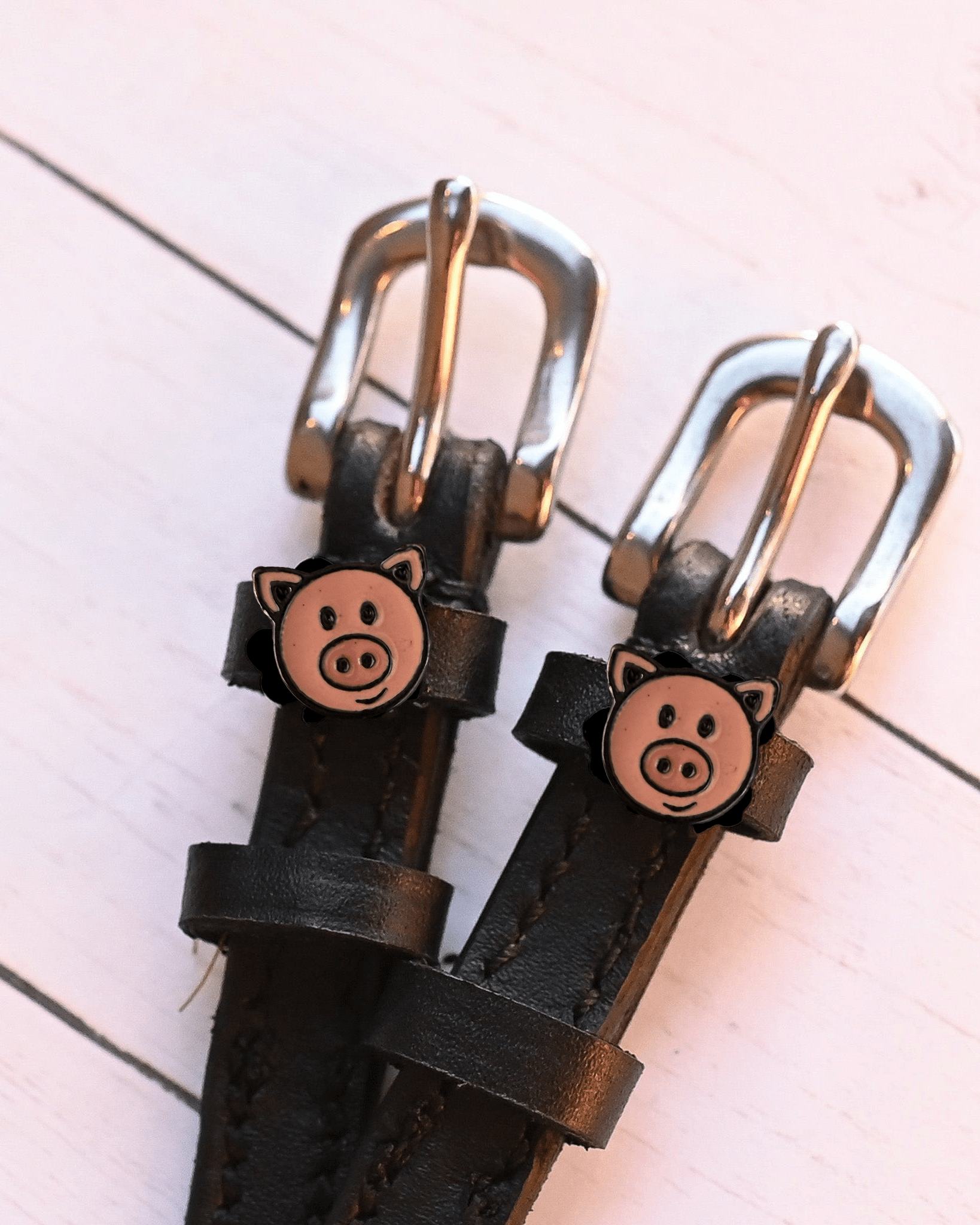 Close-up of pink pig-face charms and silver buckles on black spur straps, pink planks
