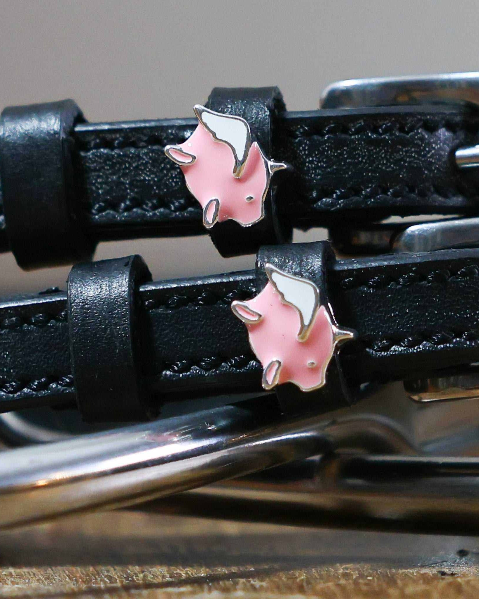 Close-up of pink winged pig charms on black leather spur strap keepers by a stirrup