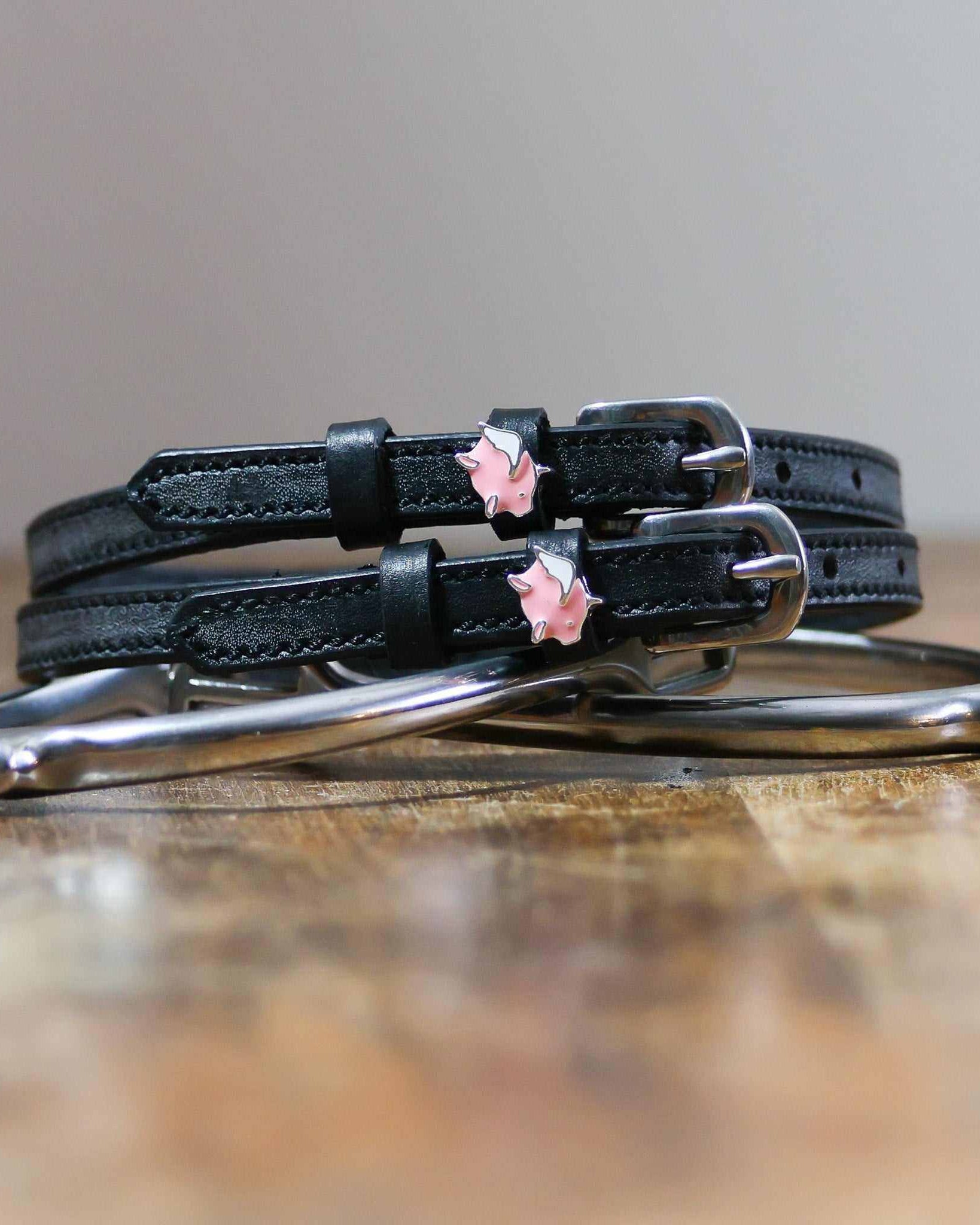 Black leather flying pig spur straps coiled beside a stirrup on wood