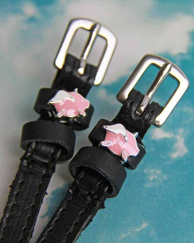 Angled close-up of winged pig charms on ManeJane spur straps against a cloudy sky