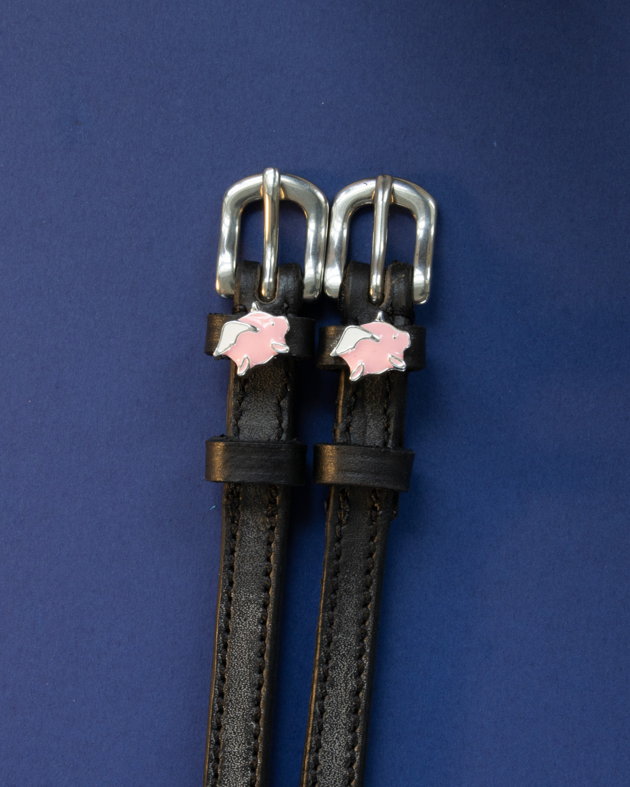 Black leather ManeJane flying pig spur straps on a navy background