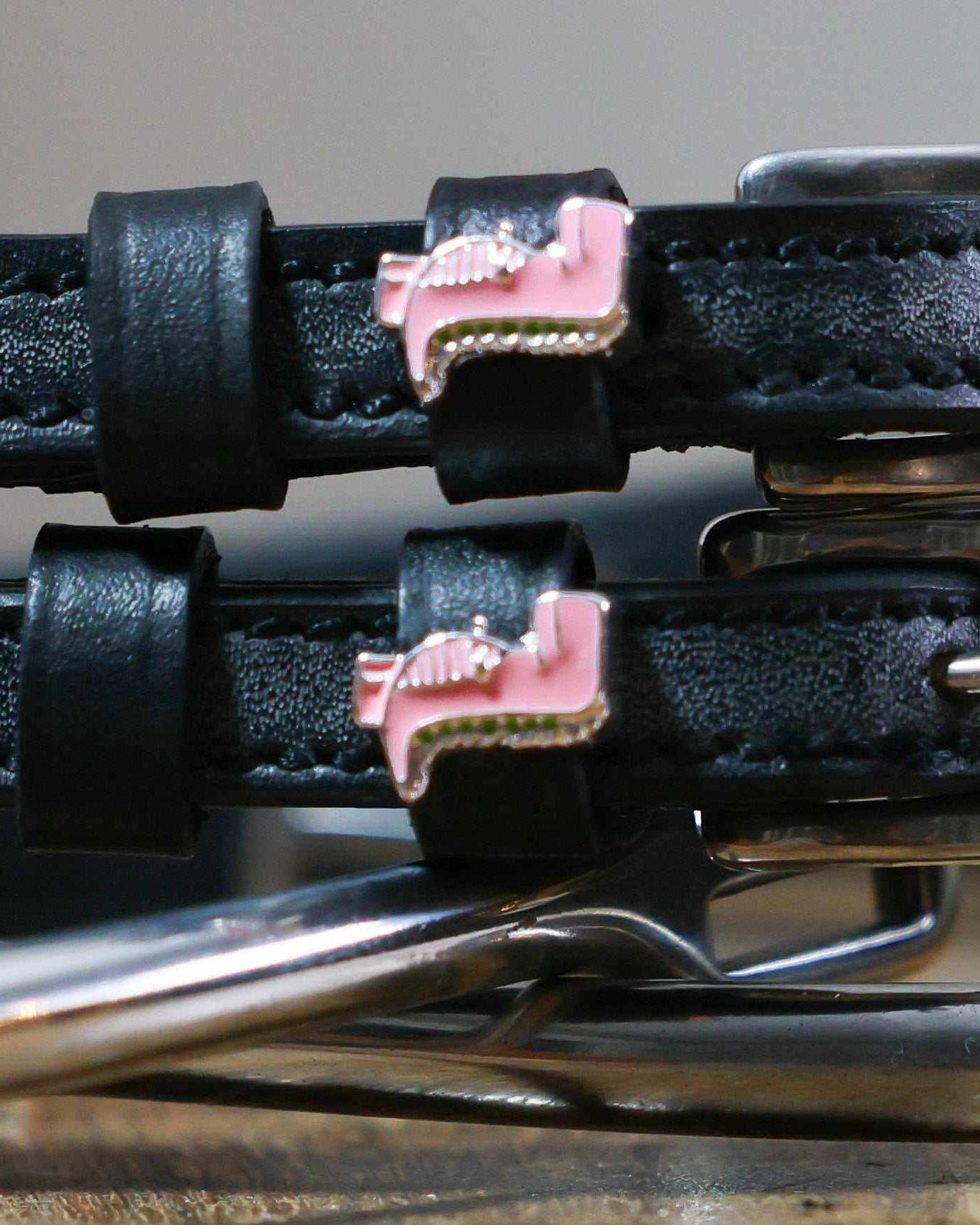 Close-up of pink T-rex dinosaur charms on black leather spur strap keepers